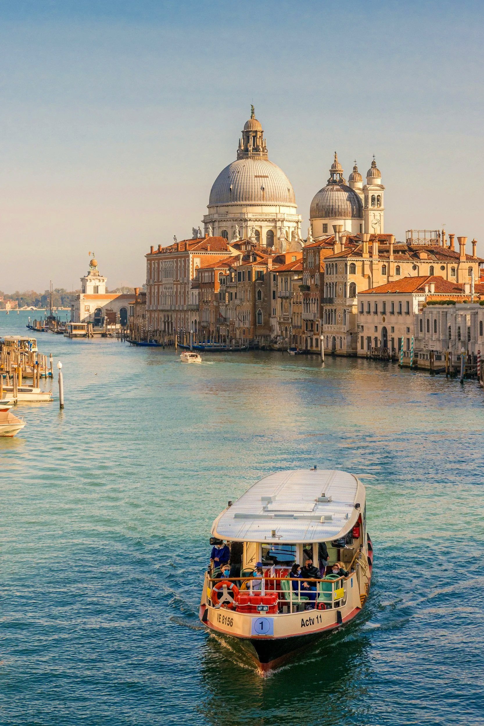 Vista del canal de Venecia con un barco de turistas navegando frente a edificios históricos, incluyendo la Basílica de Santa María della Salute.