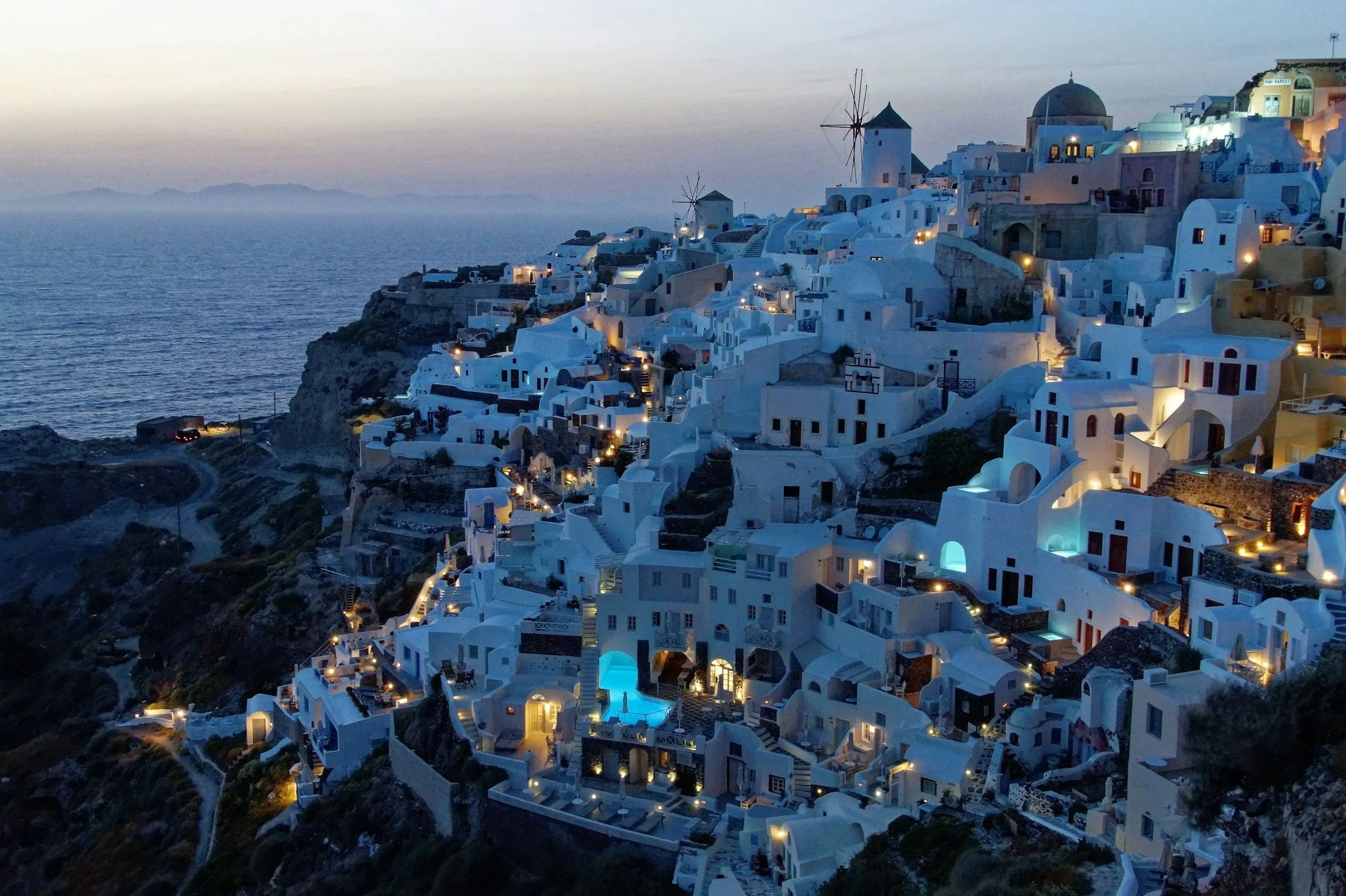Vista nocturna de las casas blancas en Santorini con el mar y el horizonte al fondo.