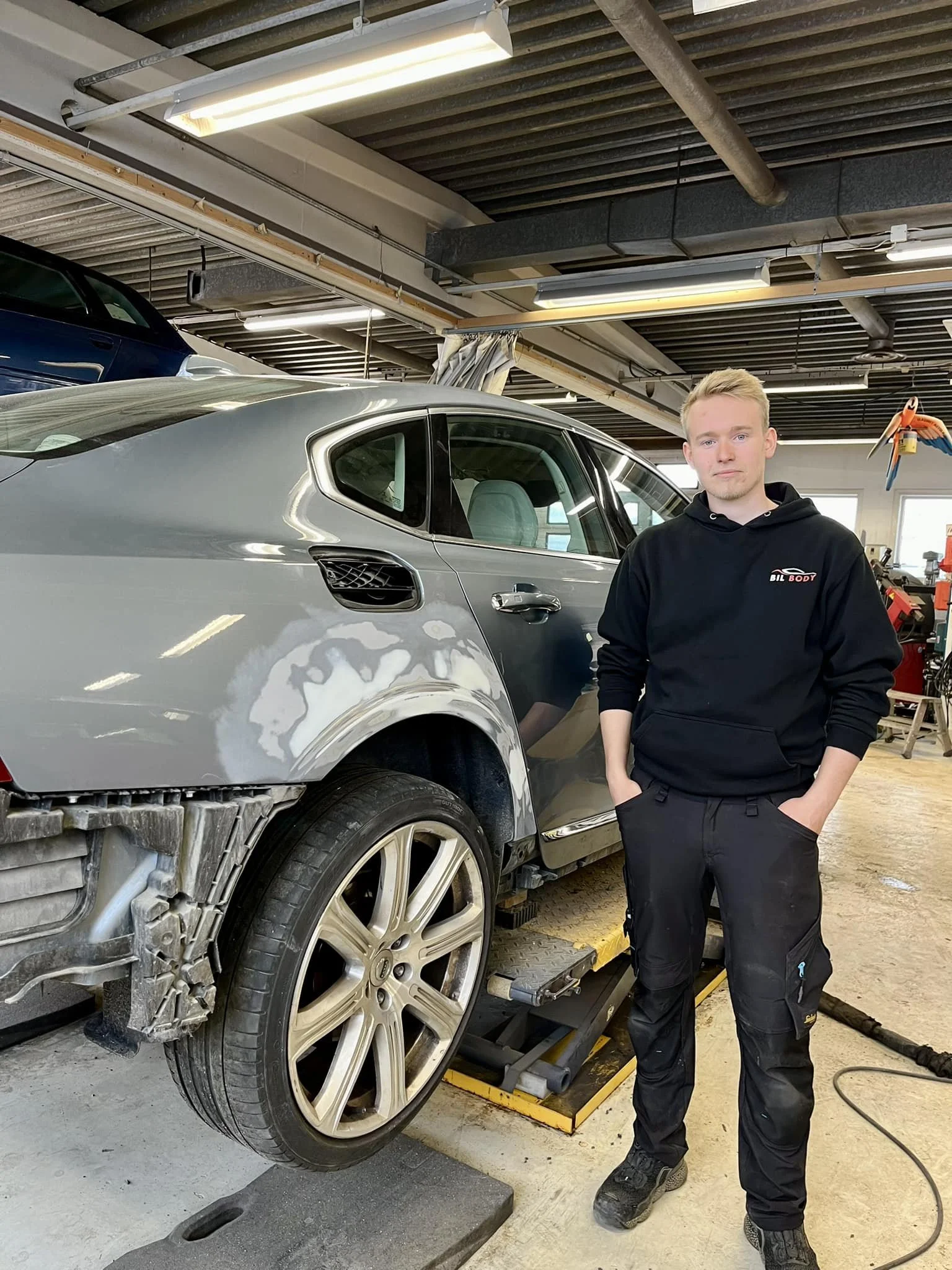 En mann står ved siden av en bil som er under reparasjon i et verksted.