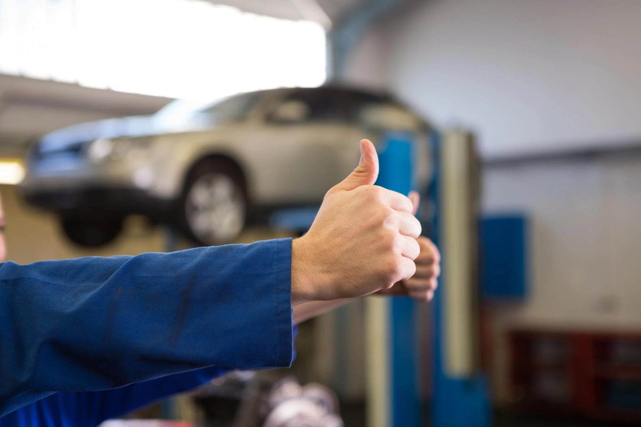 En person gir tommel opp i en bilverksted med en bil hevet over bakken.