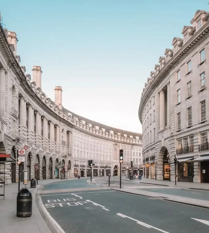 Regent street empty with white historic buildings, traffic lights, and a bus stop in London during daytime.