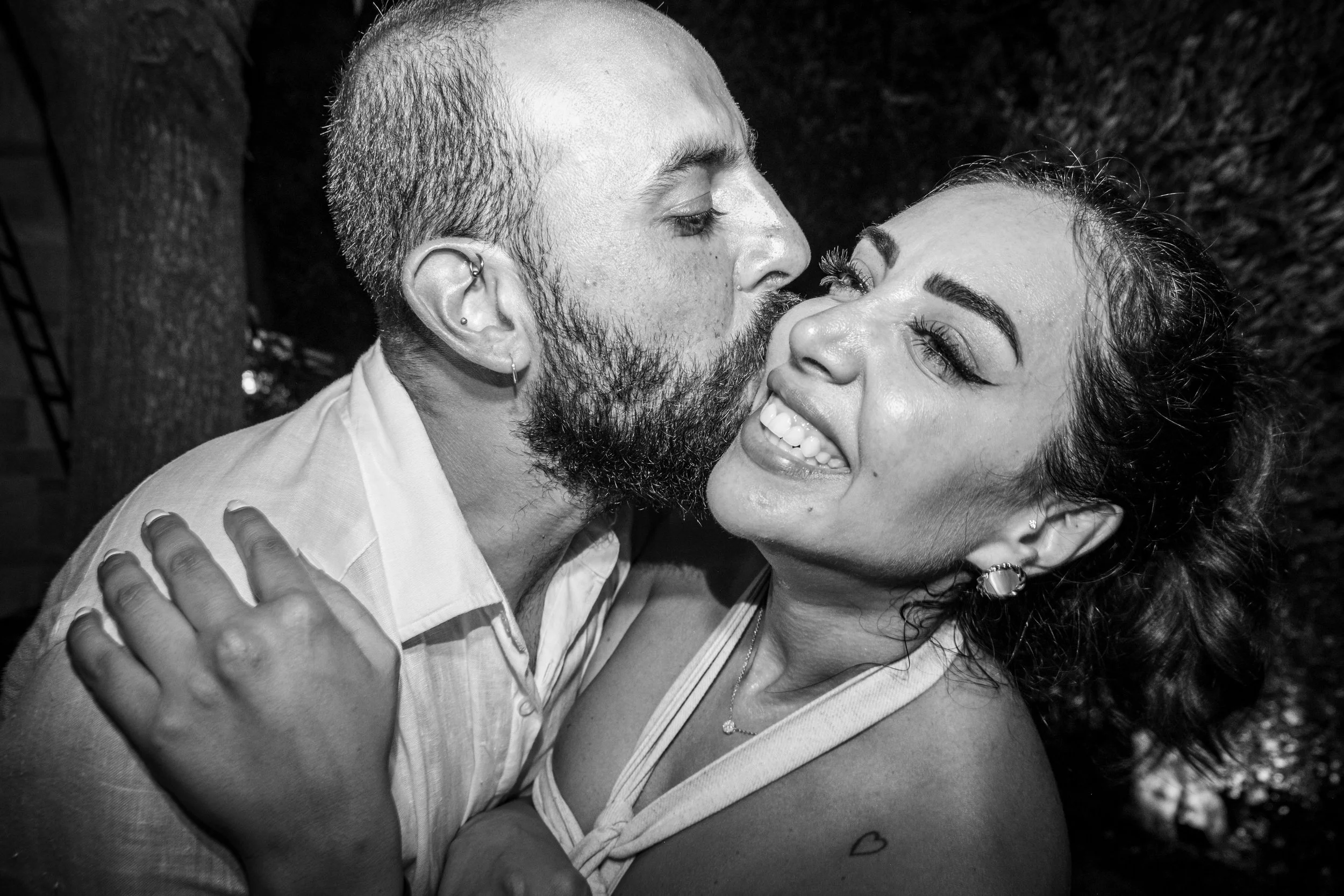 A black and white photo of a couple embracing and about to kiss, smiling and showing affection.