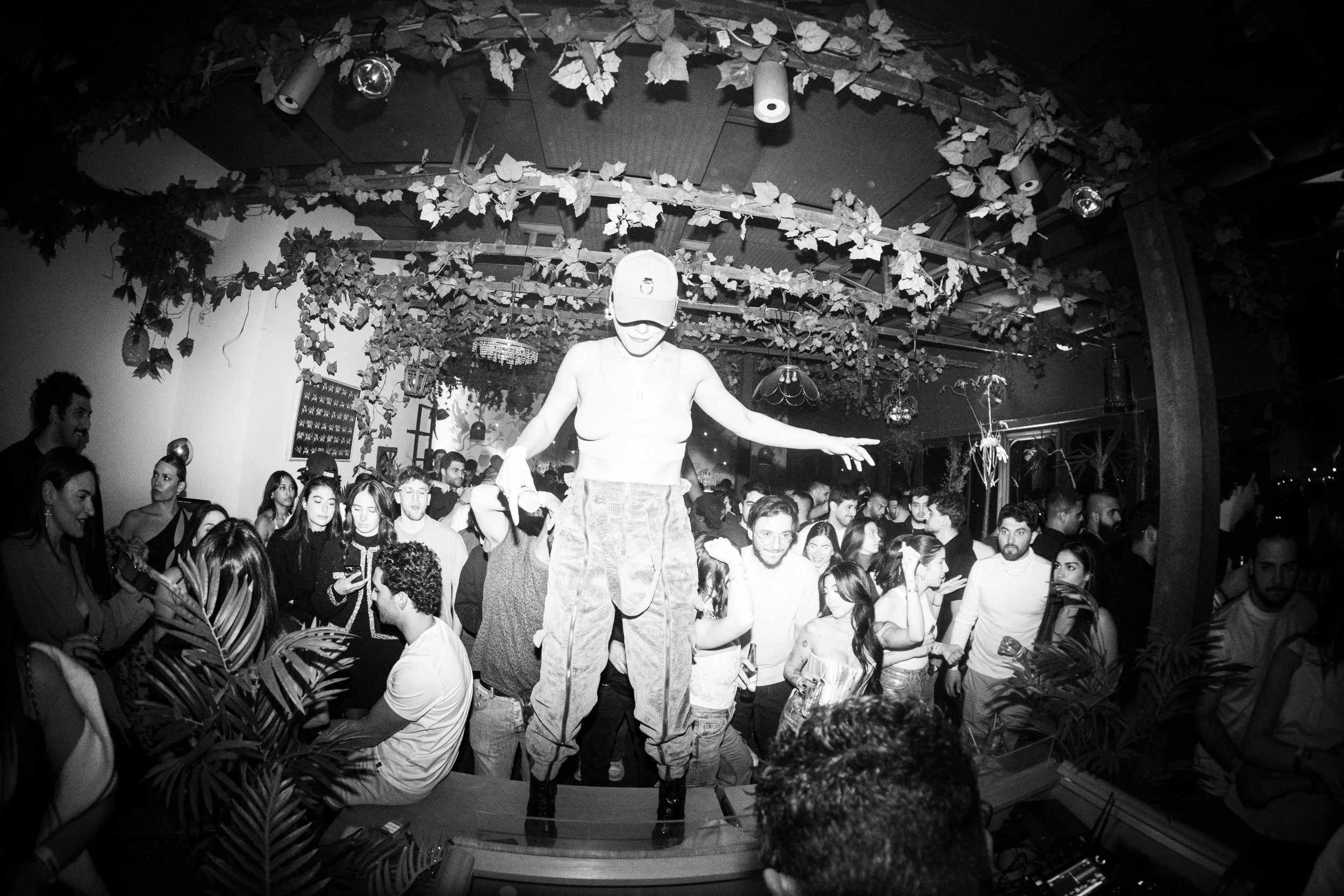 People dancing at a crowded party with a woman on stilts in the foreground