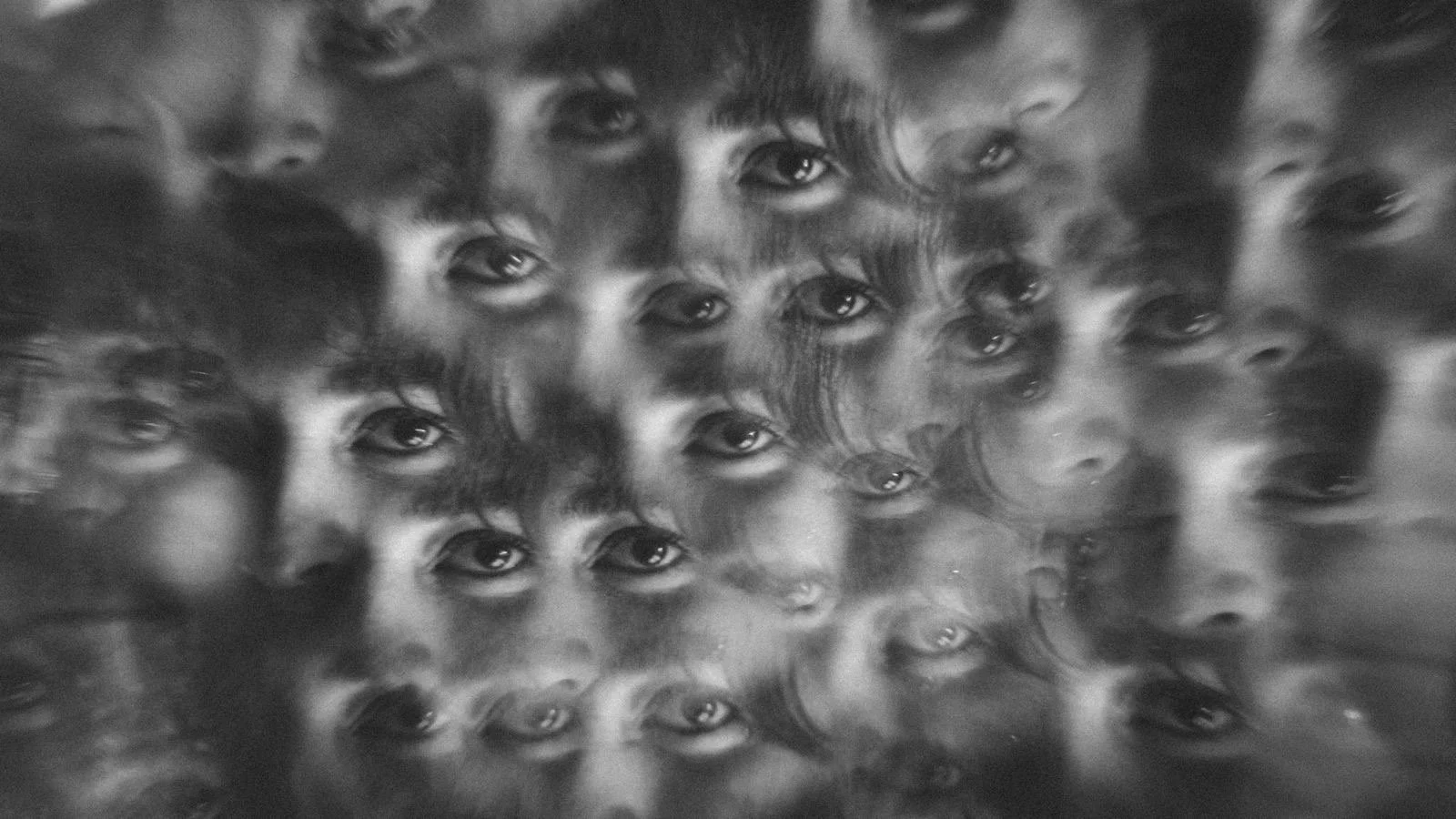A black and white abstract photo featuring multiple overlapping faces of children with expressive eyes, creating a layered, kaleidoscope-like effect.