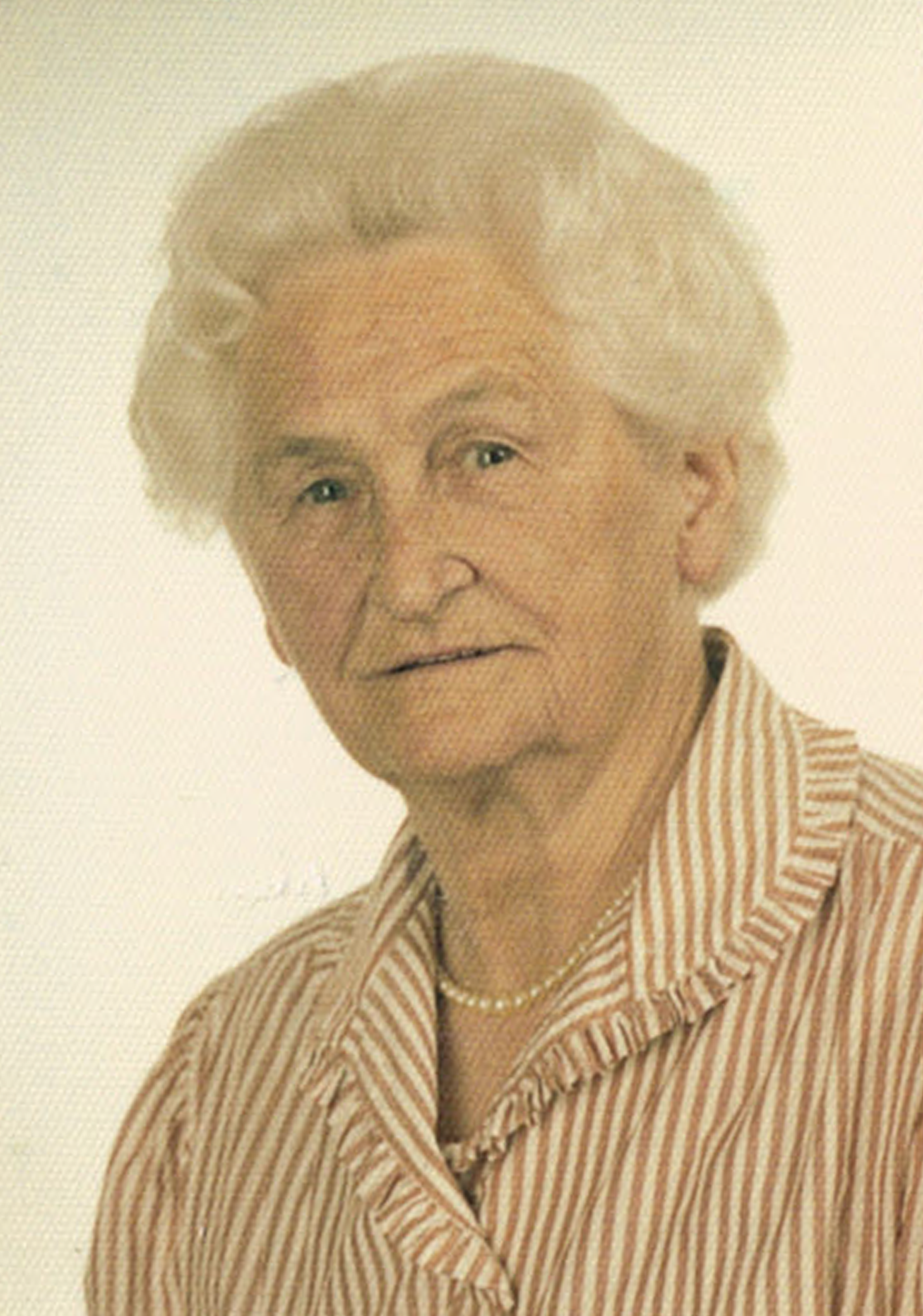 Porträt einer älteren Frau mit blonden, gelockten Haaren, trägt eine gestreifte Bluse und eine Perlenkette.