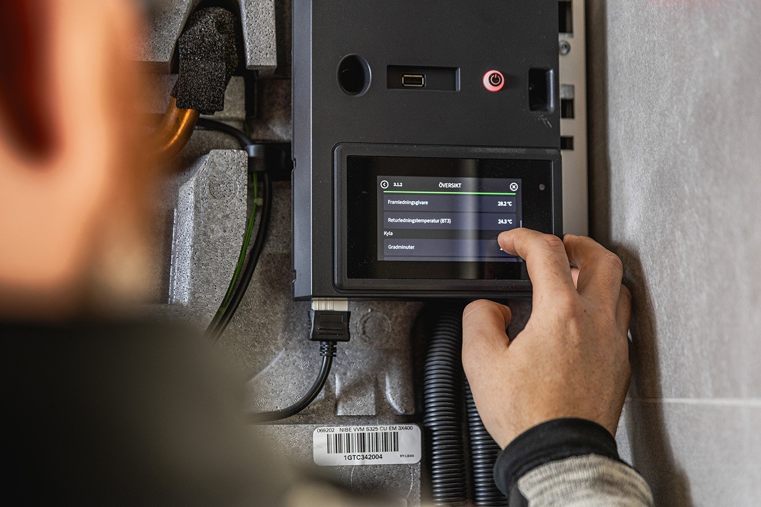 En person som justerar en digital kontrollpanel för ett tekniksystem, med visad skärm som visar temperaturer och annan data.