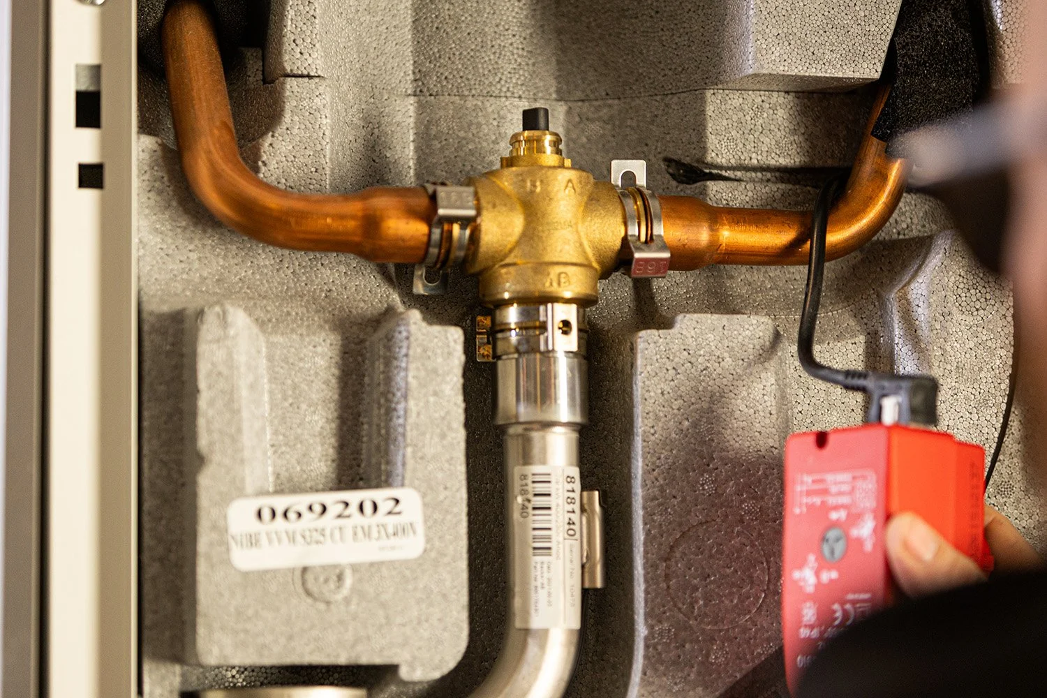 Installationsbeläggning med kopparrör, ett ventilreglage, ett rött elektriskt styrelement och isoleringsmaterial.