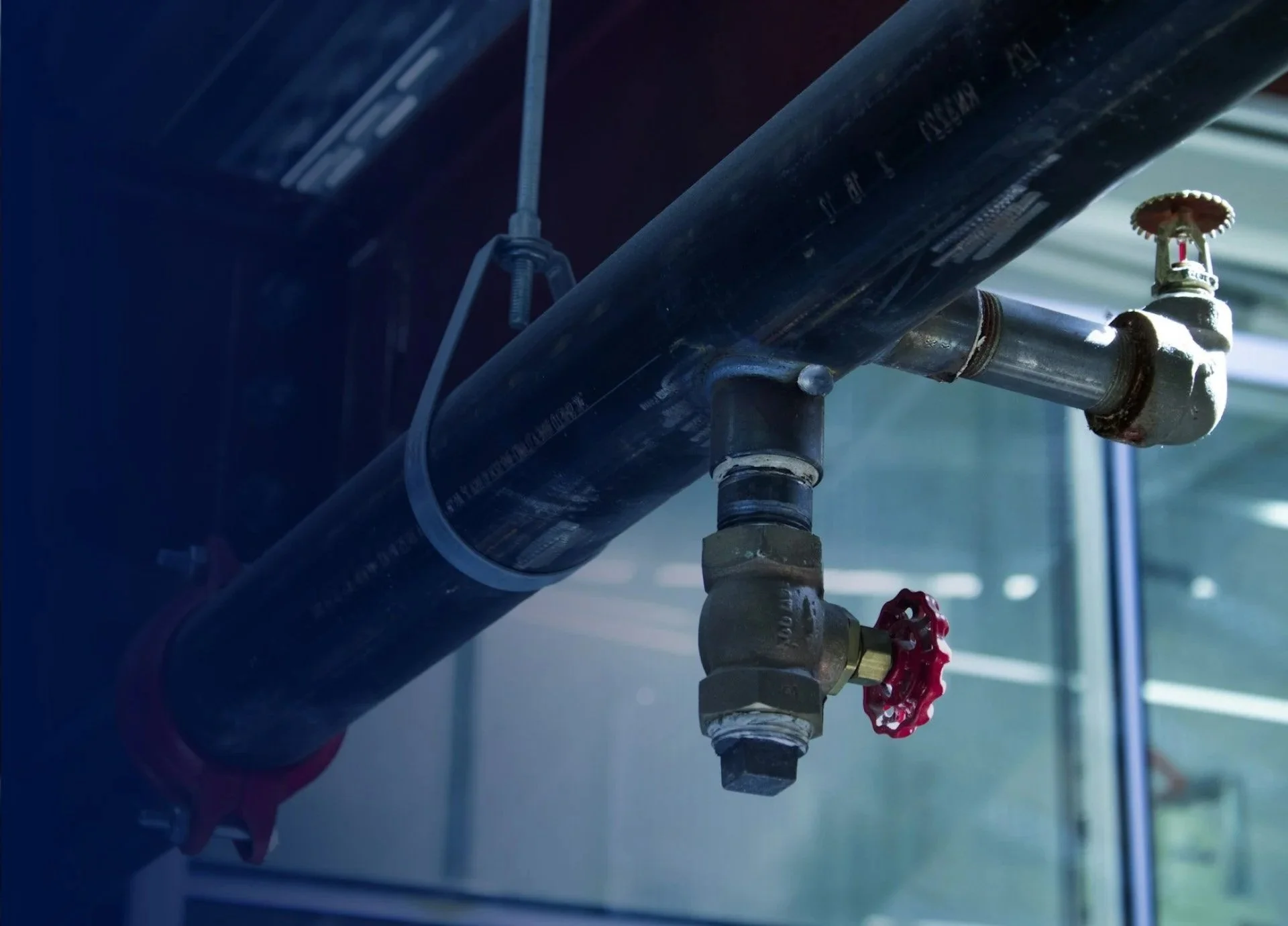 En svart rörledning med en röd ventilkoppling, installerad i ett inomhusmiljö med glasväggar.