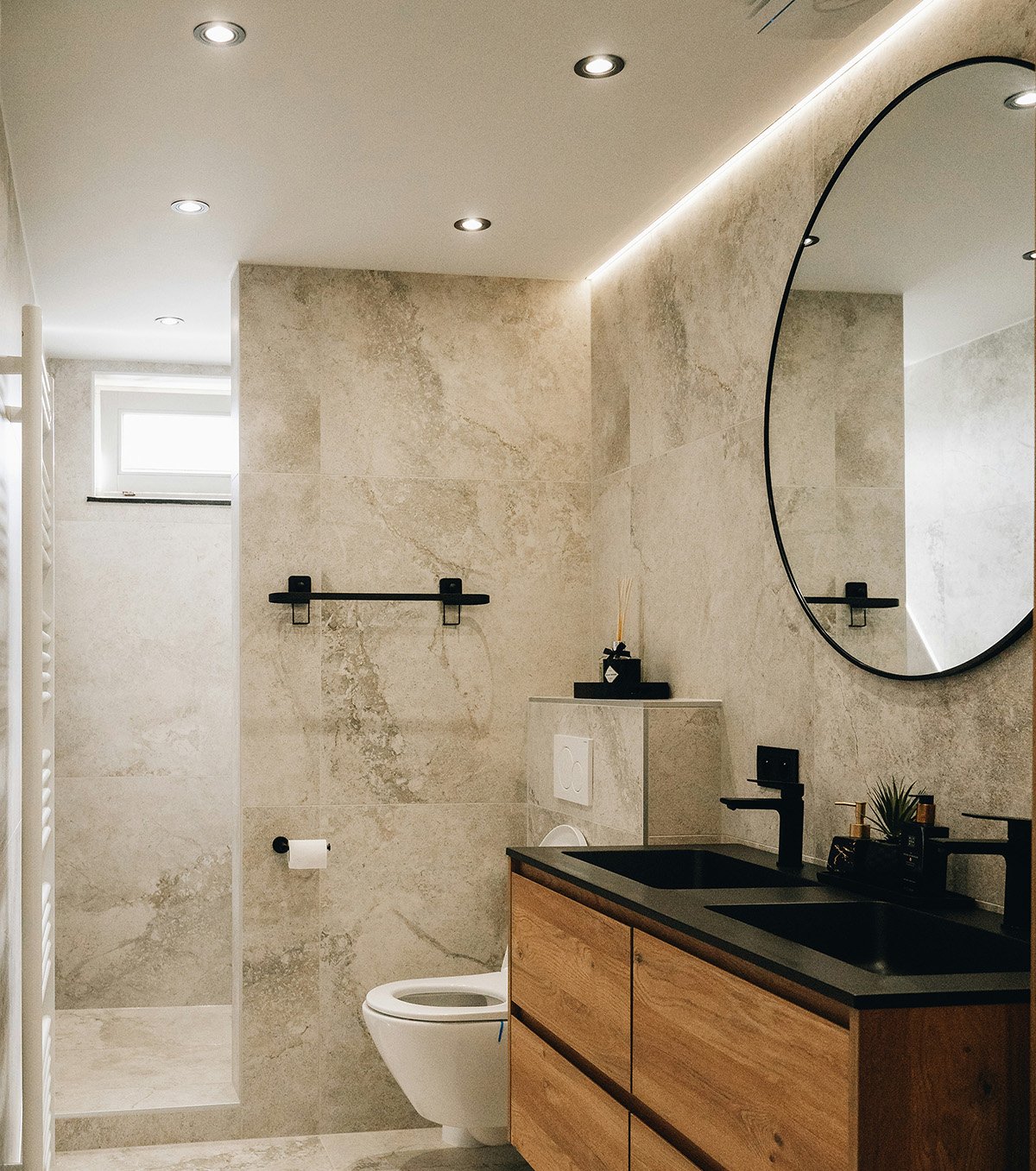 Modern badrum med beige kakelväggar, svart handfat, spegel och träskåp.