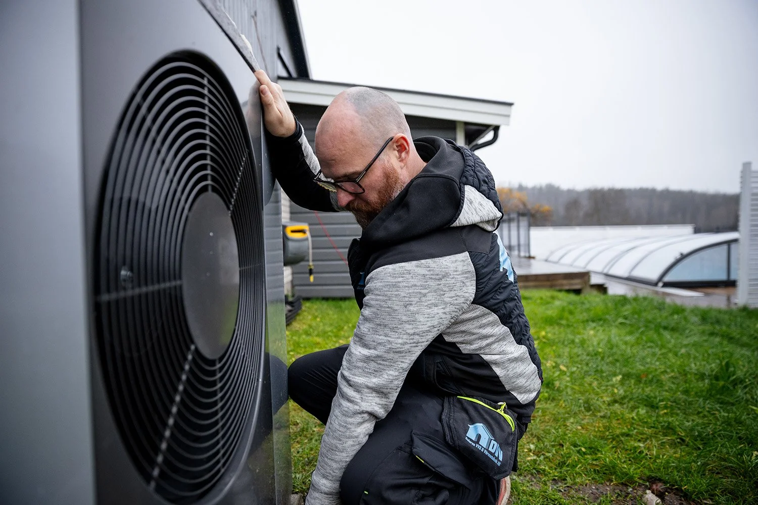 En man utför reparation på en utomhusenhet av en luftvärmepump eller luftkonditioneringssystem.