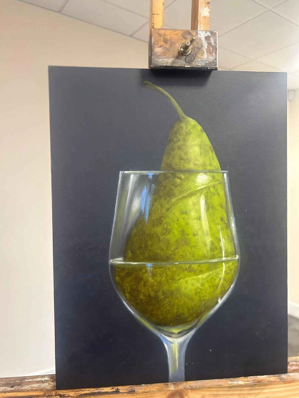 Painting of a green pear inside a transparent wine glass with a dark background.