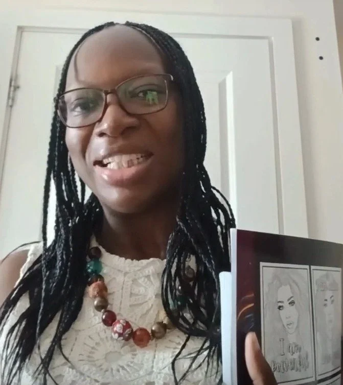 Ruthy Michaels, holding a booklet with sketches and the words 'I love you' visible on the cover, standing in front of a white door.