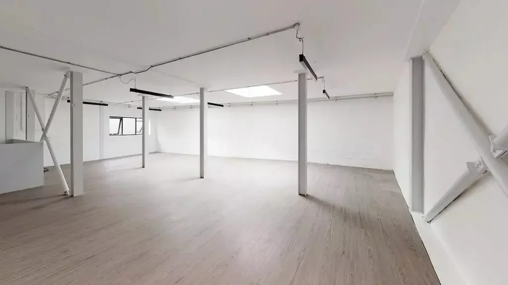Empty, white-walled room with support beams, natural light from windows, and wooden flooring.