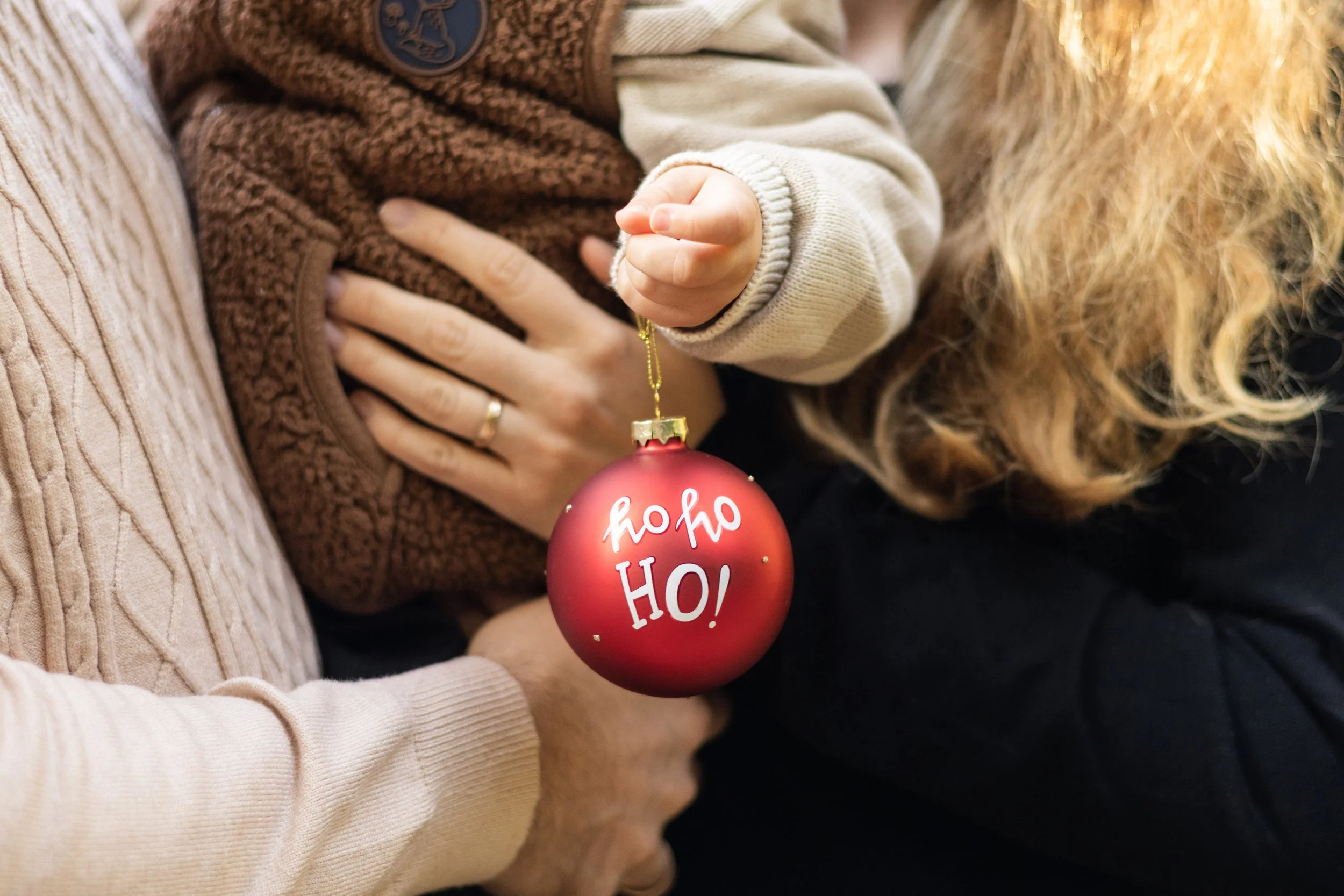 Eine Person hält einen roten Weihnachtsschmuck mit der Aufschrift 'Ho Ho Ho!' in den Händen, während eine andere Person sie umarmt. Der Schmuck ist partytauglich und festlich.