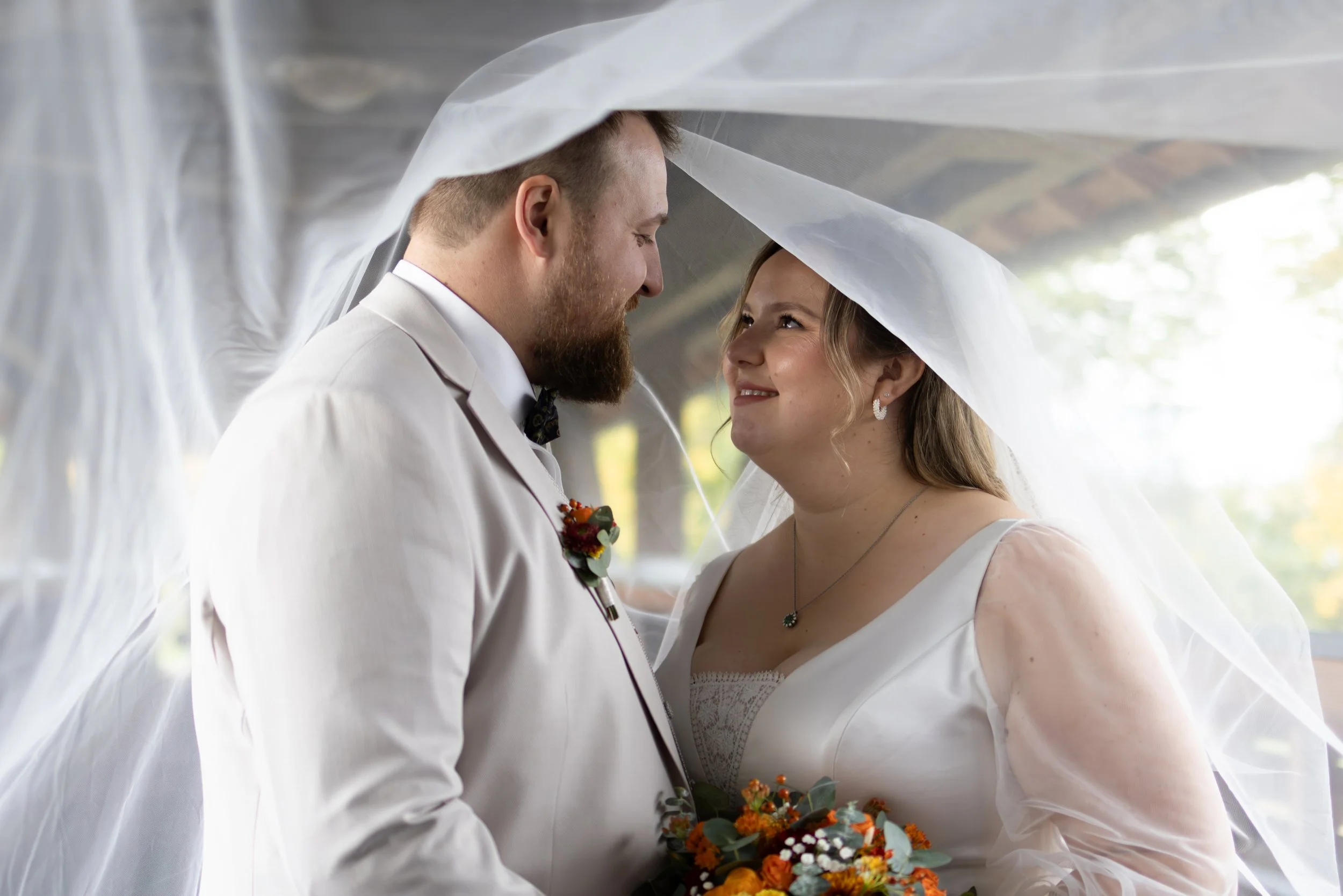 Ein Brautpaar steht sich unter dem Schleier anlächelnd bei ihrer Hochzeit.