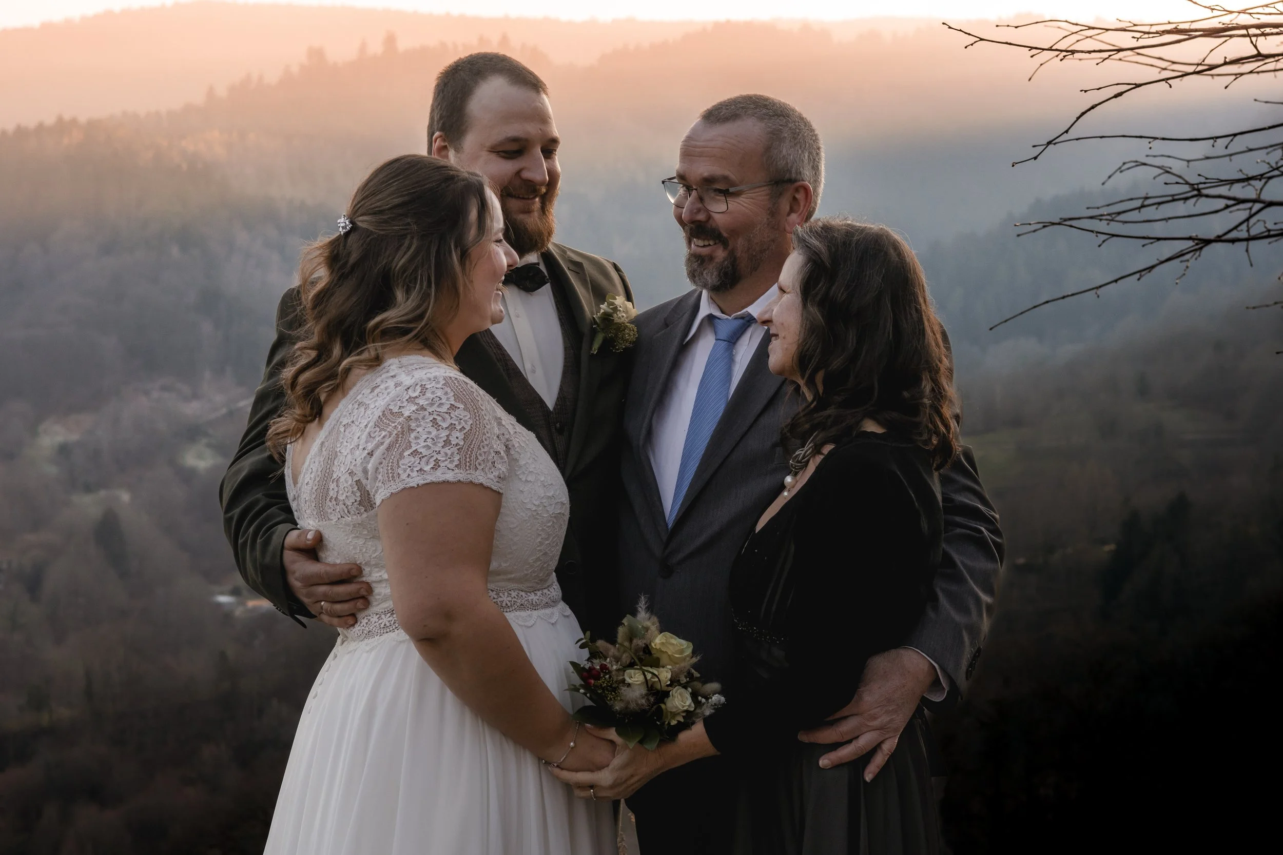 Eine Gruppe von Menschen bei einer Hochzeit, die sich lieben und umarmen, vor einer natürlicher Kulisse mit Bergen bei Sonnenuntergang.