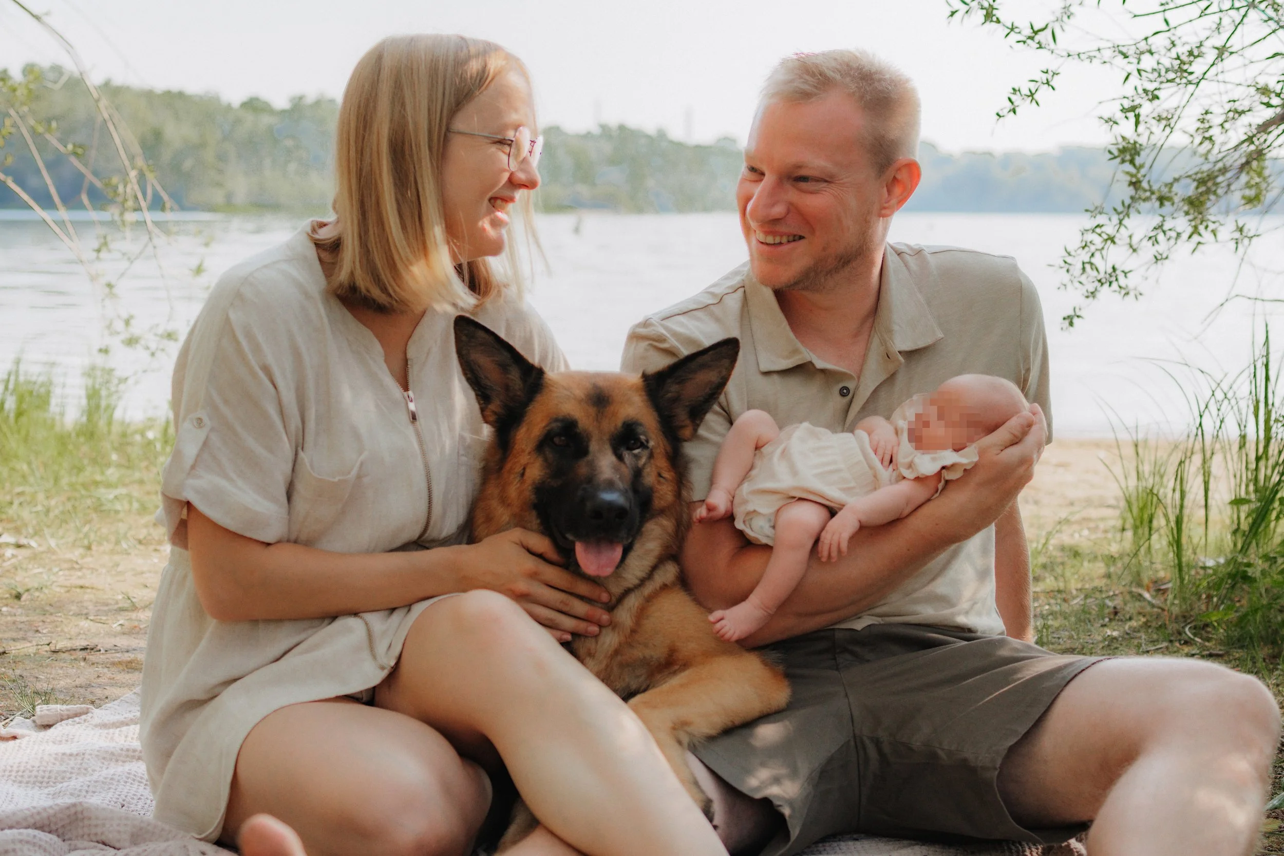 Ein glückliches Paar mit einem Hund und einem Baby am Flussufer im Freien.