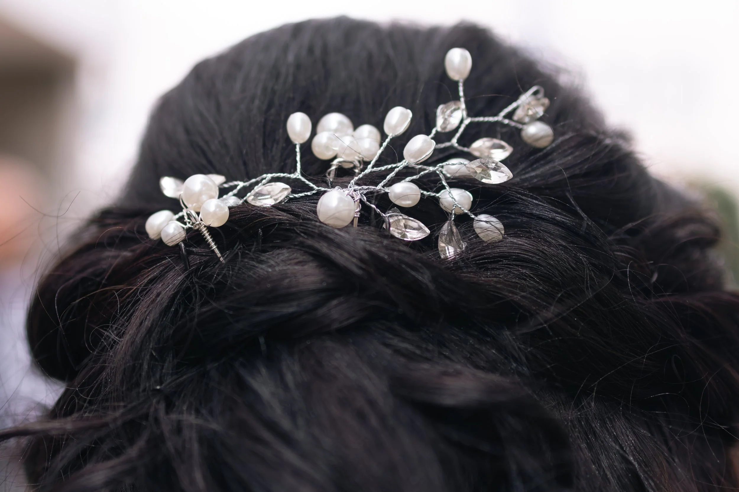 Näheaufnahme eines eleganten Haaraccessoires mit Perlen und Kristallen, das im schwarzen Haar einer Person platziert ist.