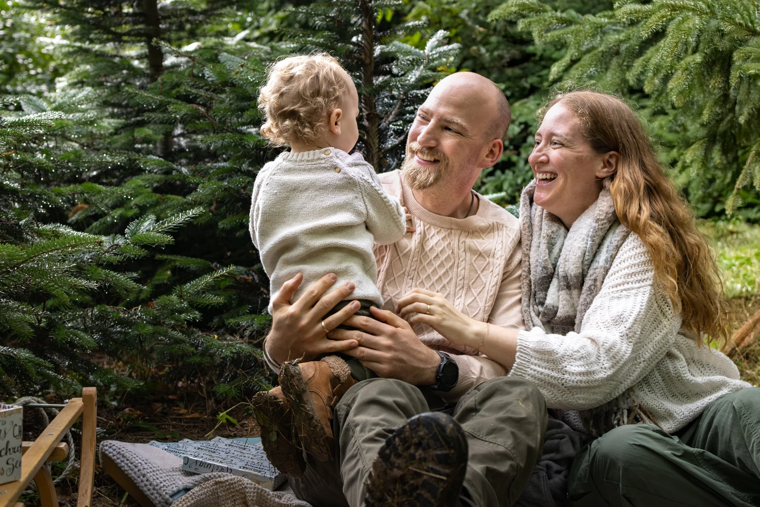 Ein glückliches Familienleben im Wald, bestehend aus einem Mann, einer Frau und einem kleinen Kind, sitzen auf einer Decke und lachen zusammen