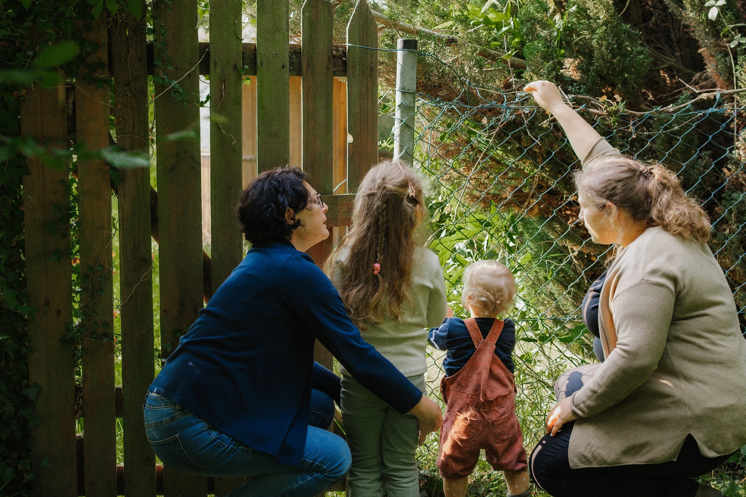 Vier Menschen, zwei Erwachsene und zwei Kinder, betrachten ein Tier im Gehege hinter einem Maschendrahtzaun, mit einem Holz- und Metallzaun im Hintergrund.
