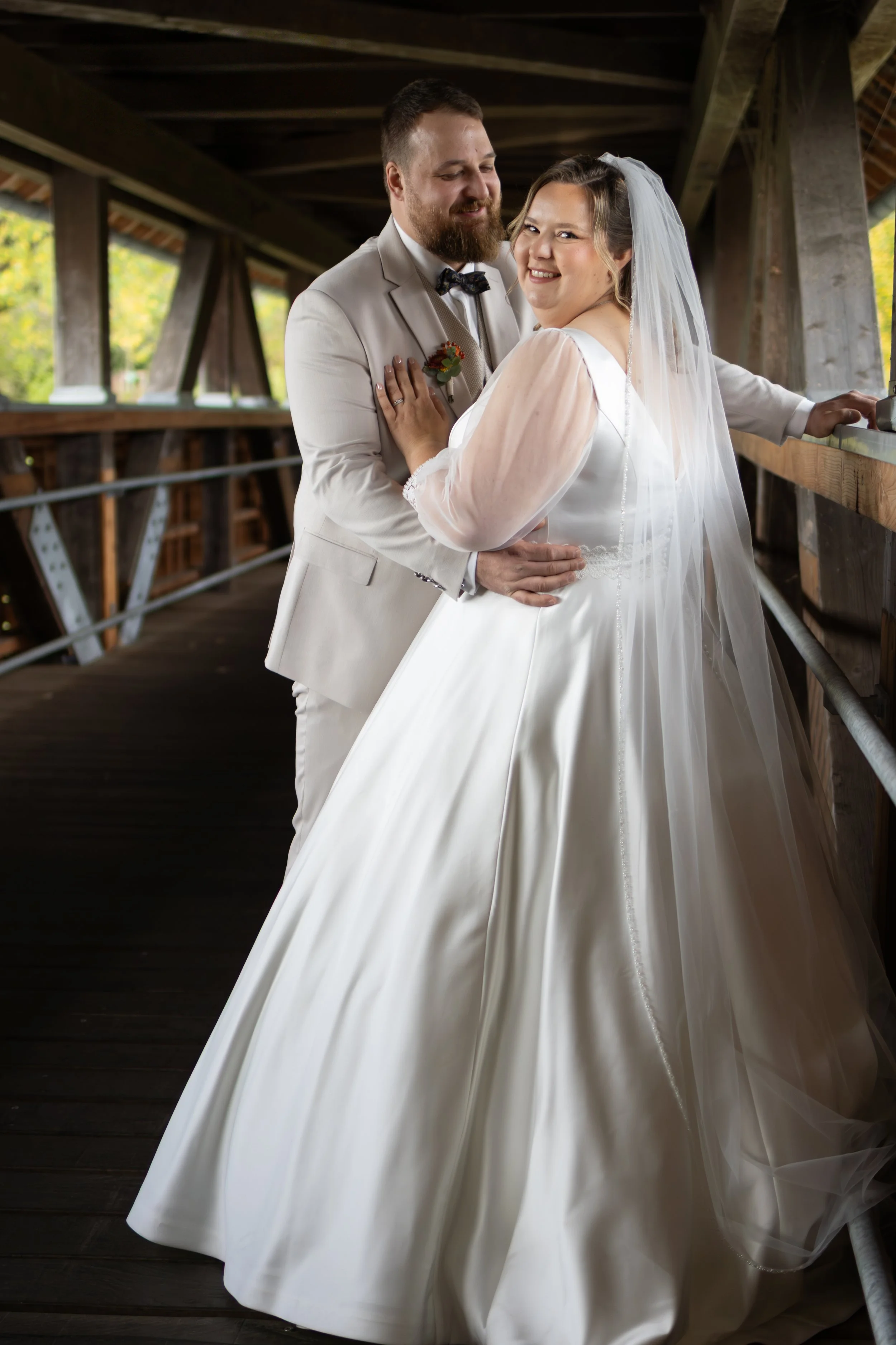 Ein Brautpaar in Hochzeitskleidung posiert in einer Holzkonstruktion, vermutlich während ihrer Hochzeitsfeier.