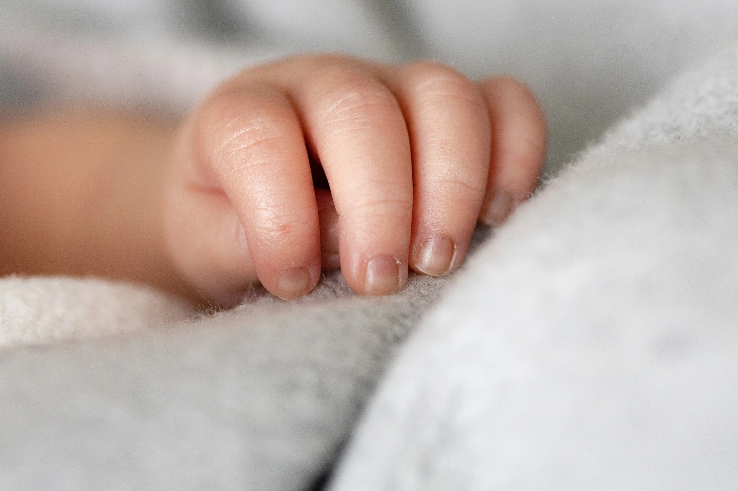 Nahaufnahme einer kleinen Kinderhand, die auf einem weichen, grauen Stoff liegt.