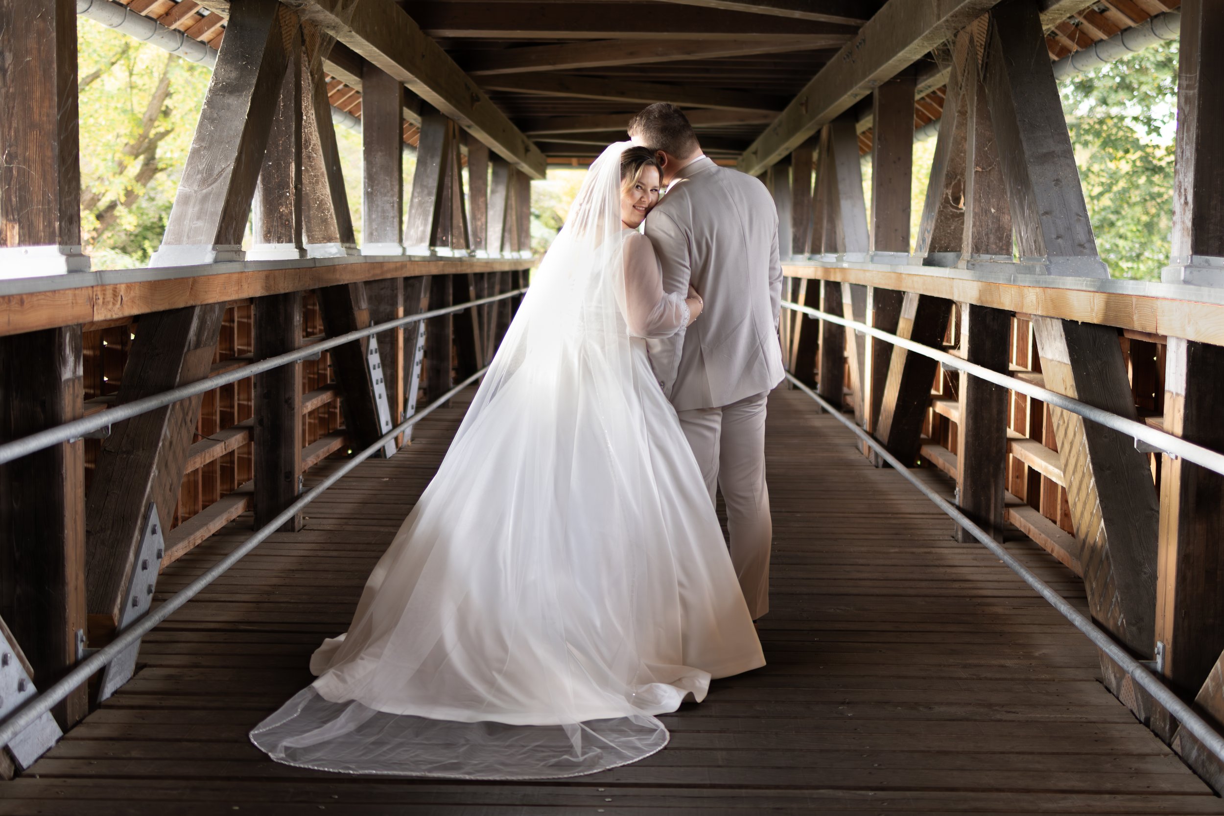 Braut und Bräutigam auf einer Holzbrücke, umgeben von Natur, bei einer Hochzeit, im Sonnenlicht