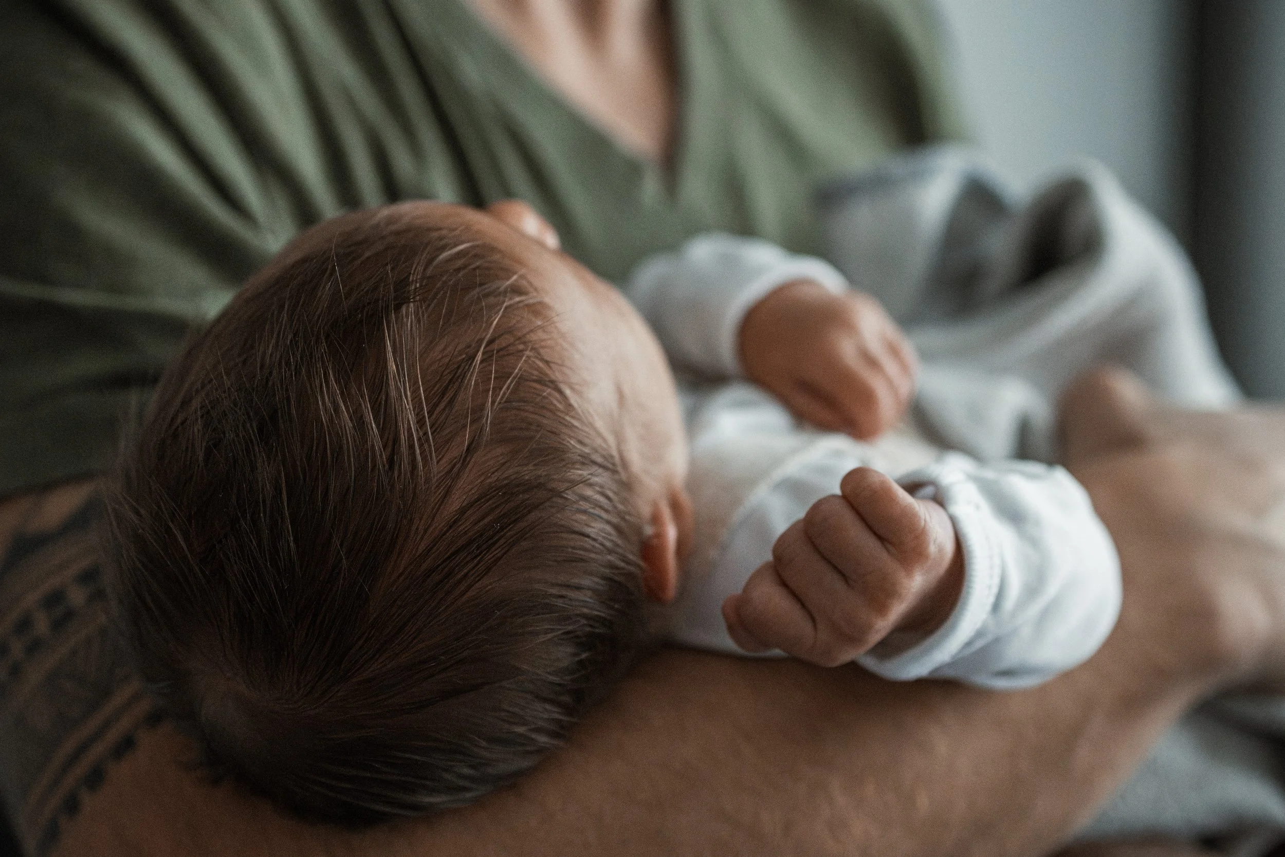 Ein Neugeborenes wird von einer erwachsenen Person gestützt, das Kind trägt weiße Kleidung und liegt ruhig auf dem Arm der Person.
