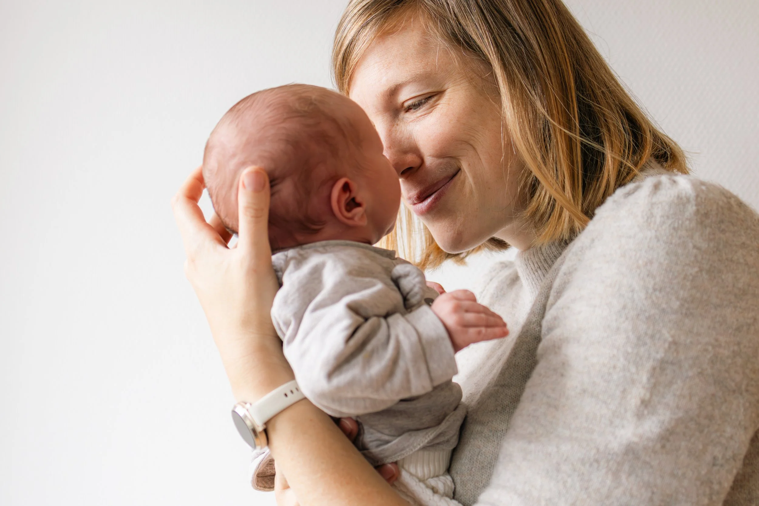 Eine Frau hält ein neugeborenes Baby hoch und beide schauen sich liebevoll an.