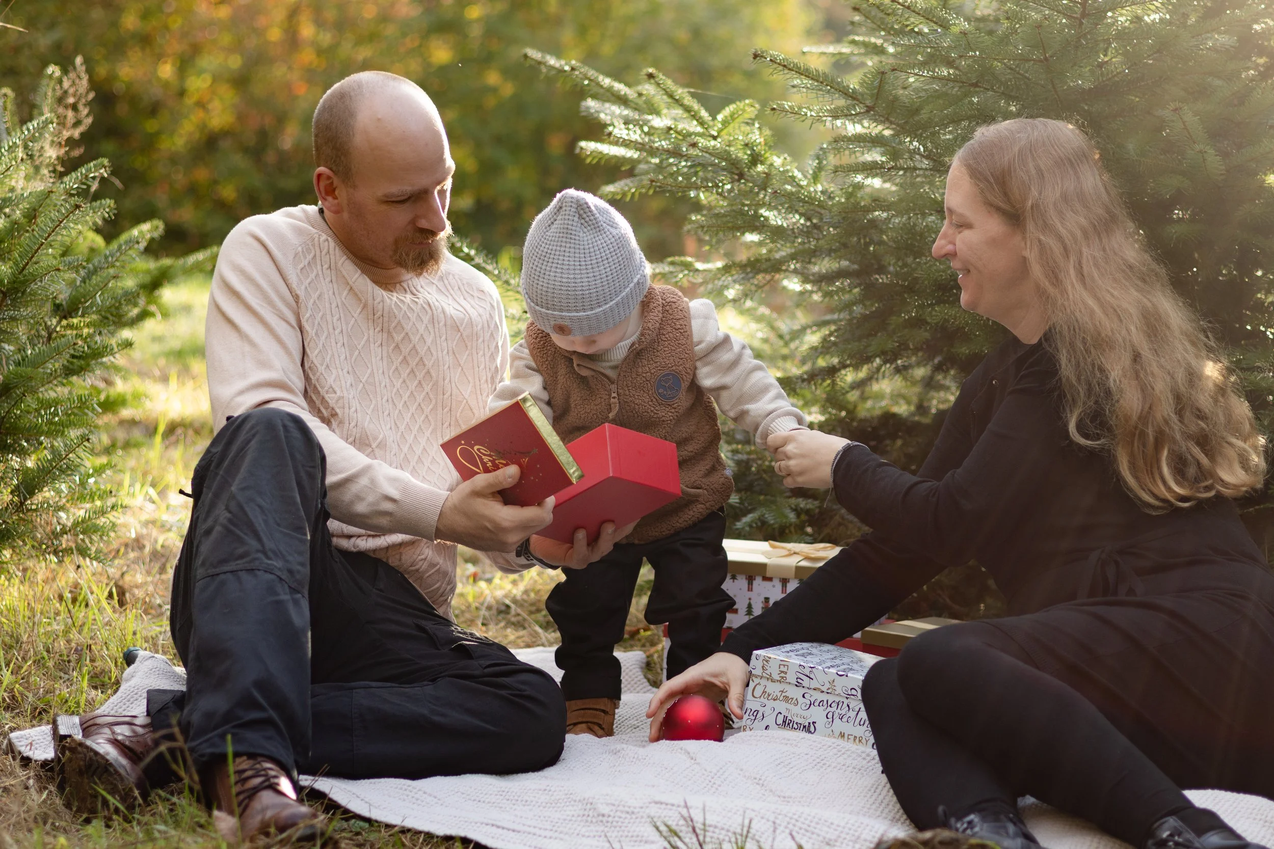 Familie beim Weihnachtsgeschenk im Freien, umgeben von Tannenbäumen.