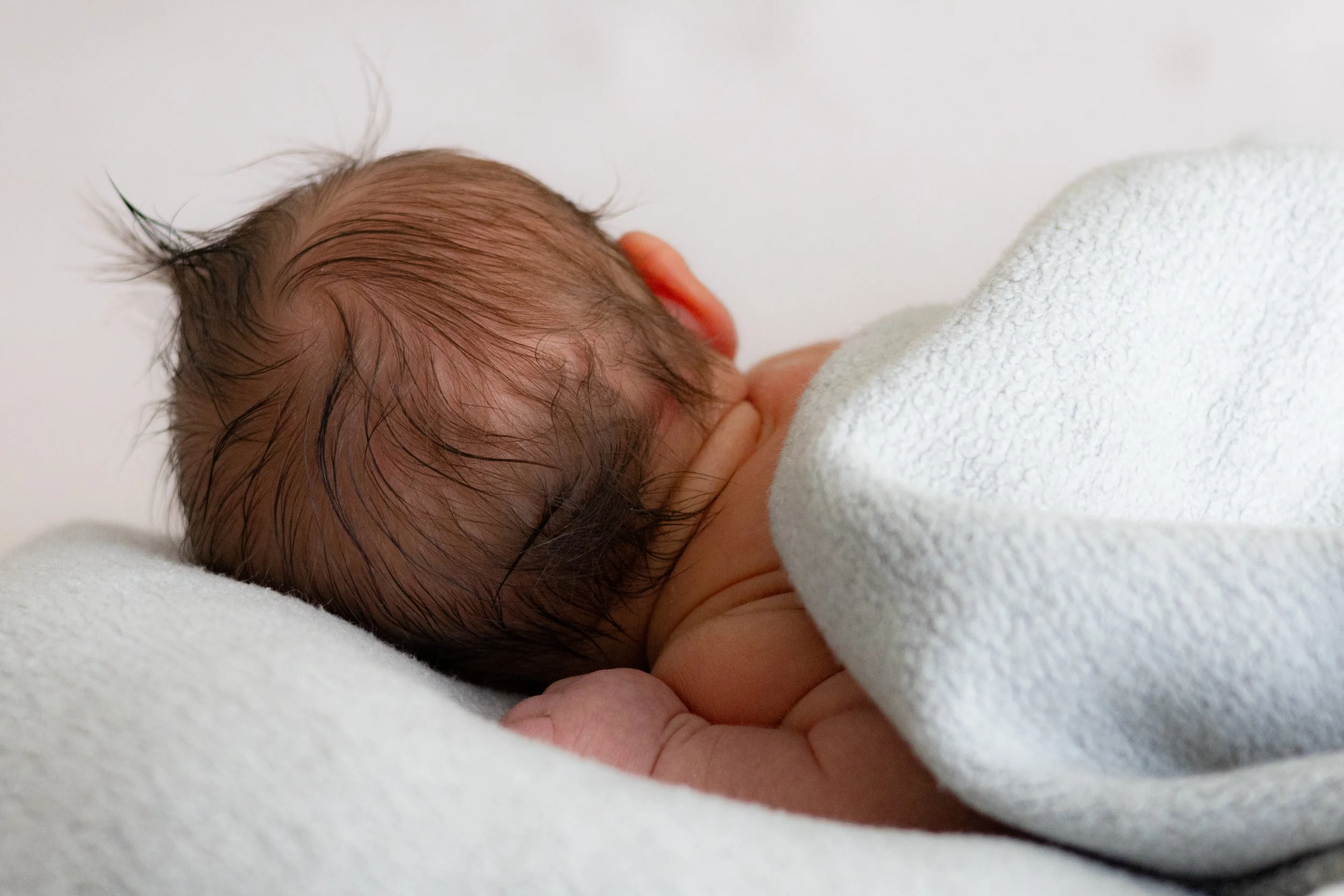 Nahaufnahme eines neugeborenen Babys, das auf einem weißen Tuch liegt, mit nassem Haaren.