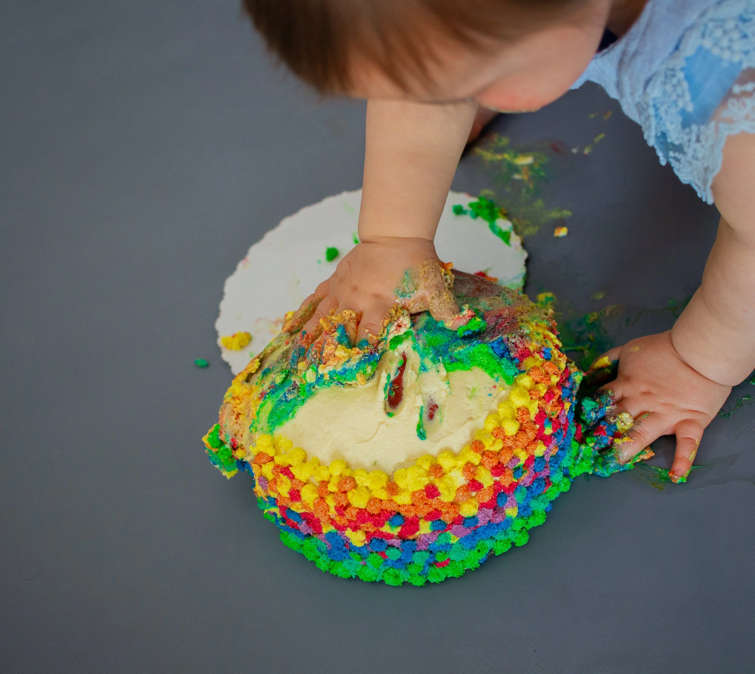 Kind beim Umarmen eines bunt dekorierten, zerbrochenen Kuchen auf einer dunklen Oberfläche.