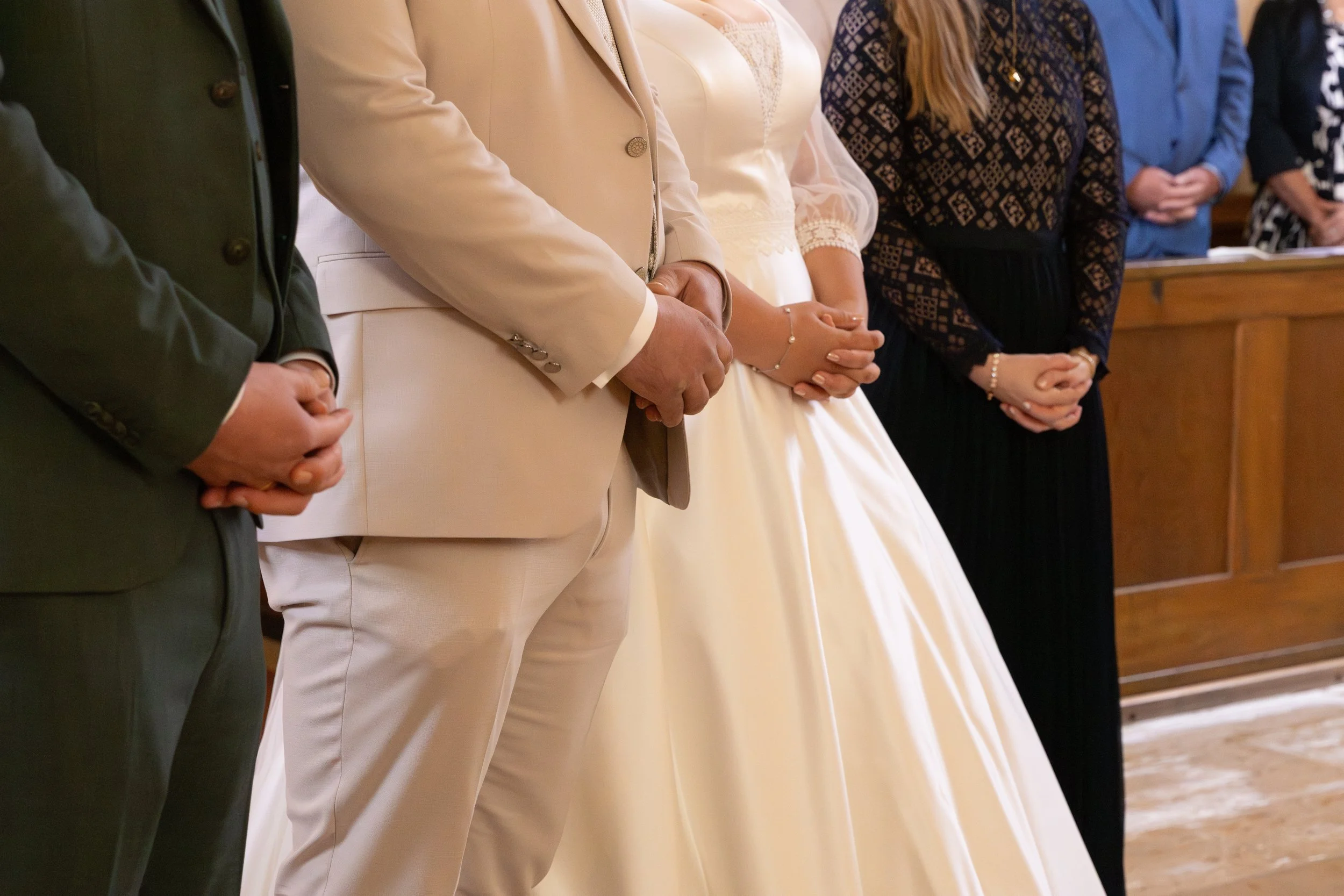 Menschen stehen bei einer Zeremonie mit gefalteten Händen, darunter ein Brautpaar in Hochzeitskleidung.