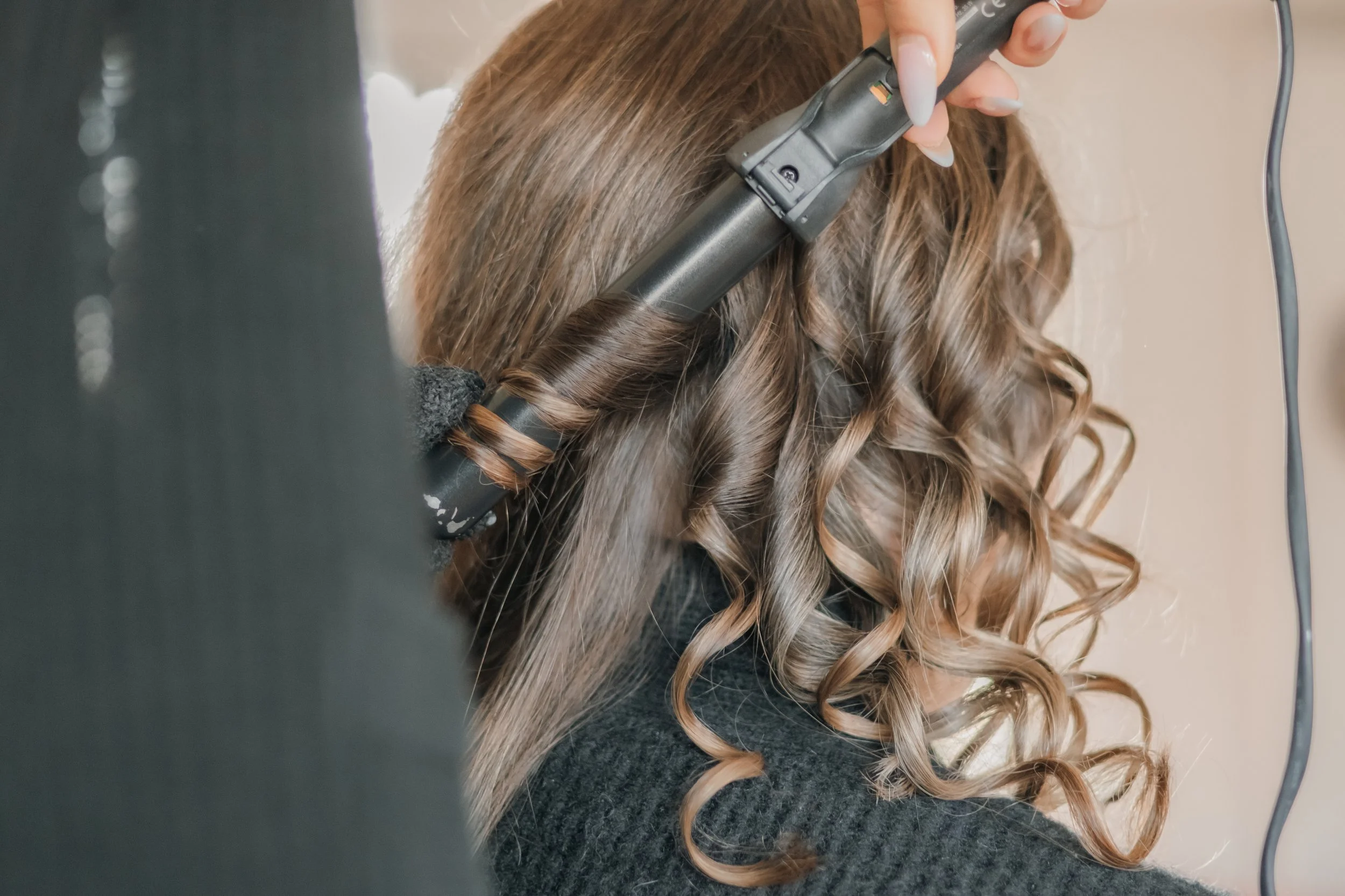 Person beim Locken ihrer braunen, gewellten Haare mit einem Lockenstab.