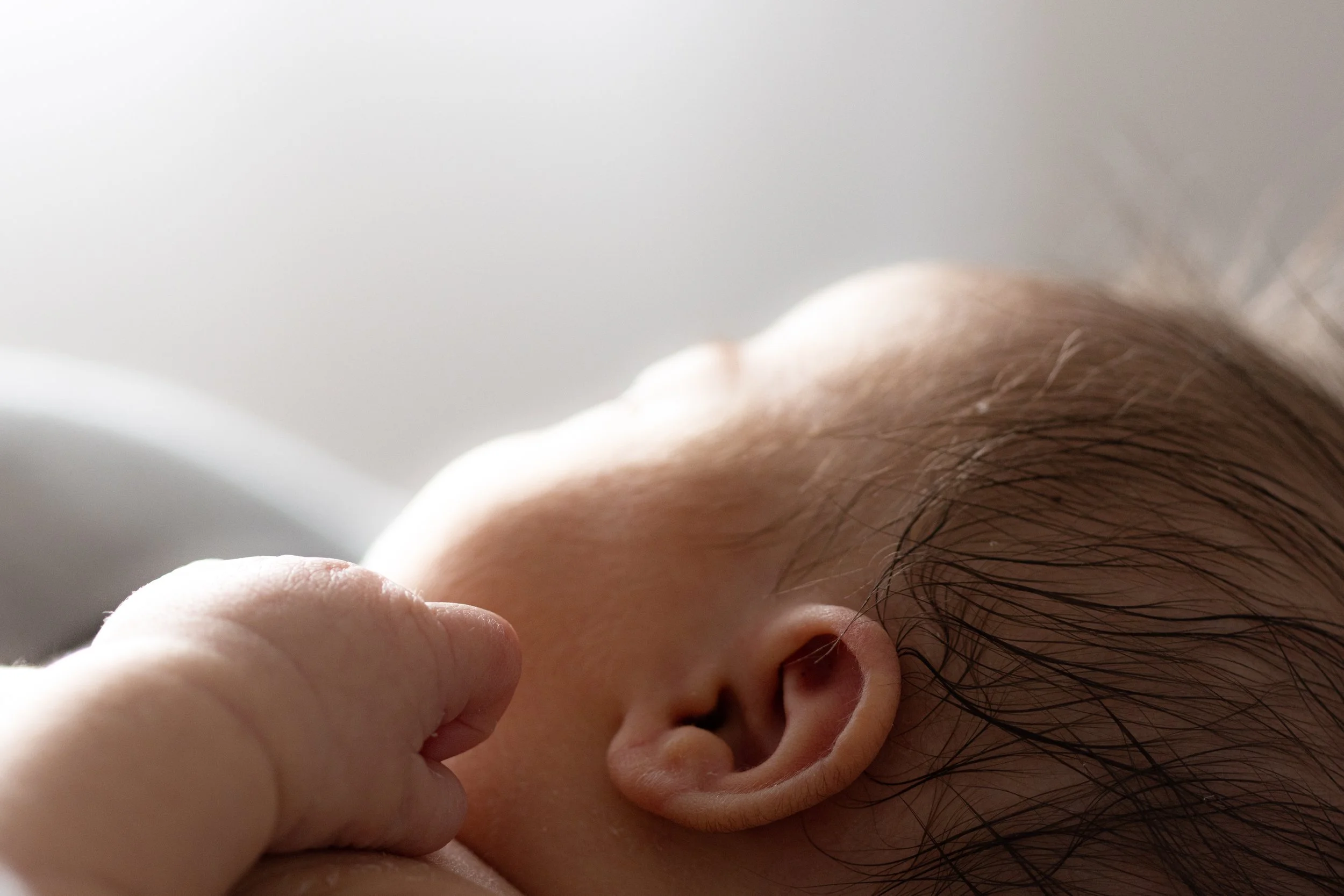 Nahaufnahme eines Neugeborenen, das an der Brust einer Person saugt, mit Fokus auf das Ohr und das Gesicht des Babys.