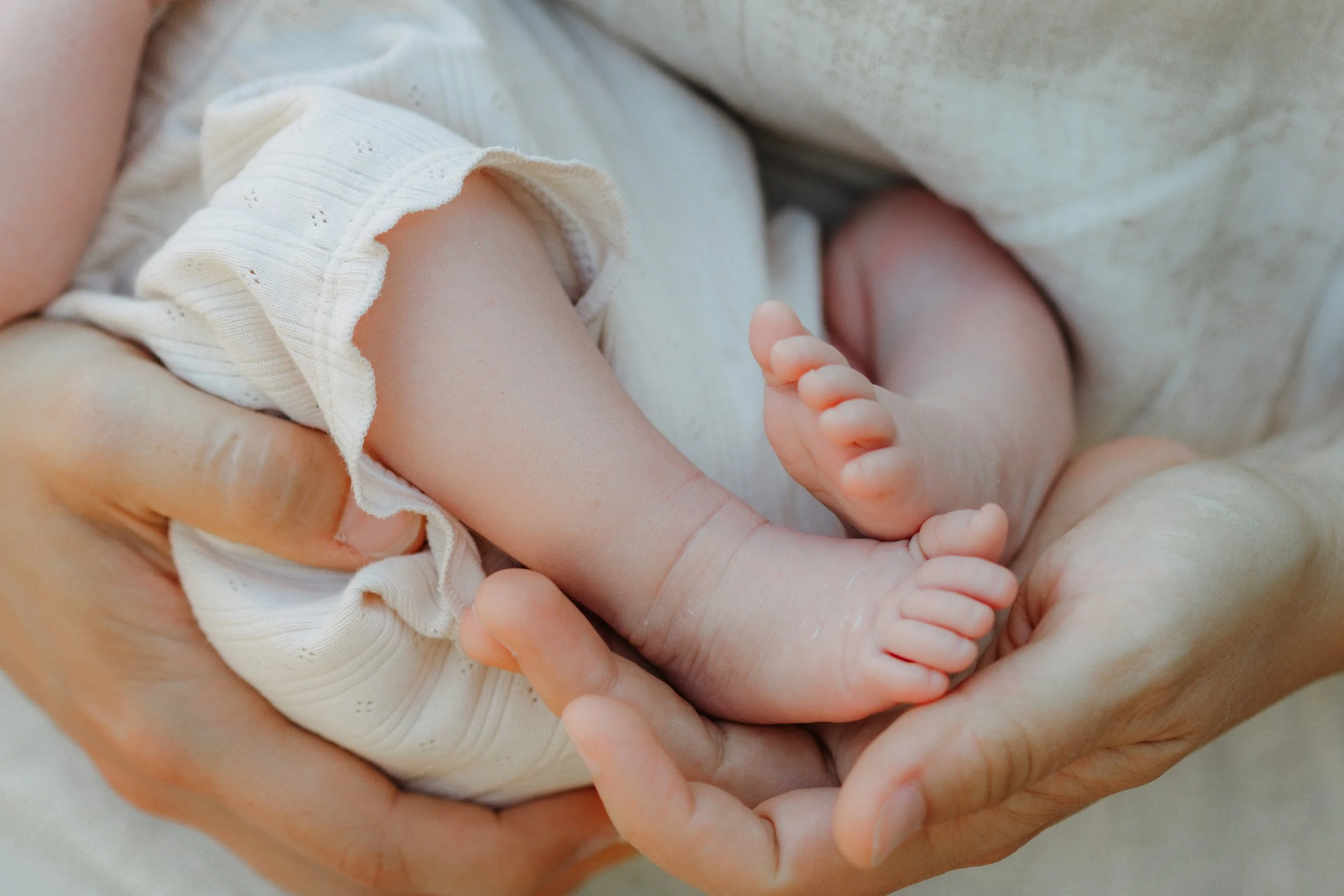 Nahaufnahme eines Babys, das in den Händen einer erwachsenen Person liegt.