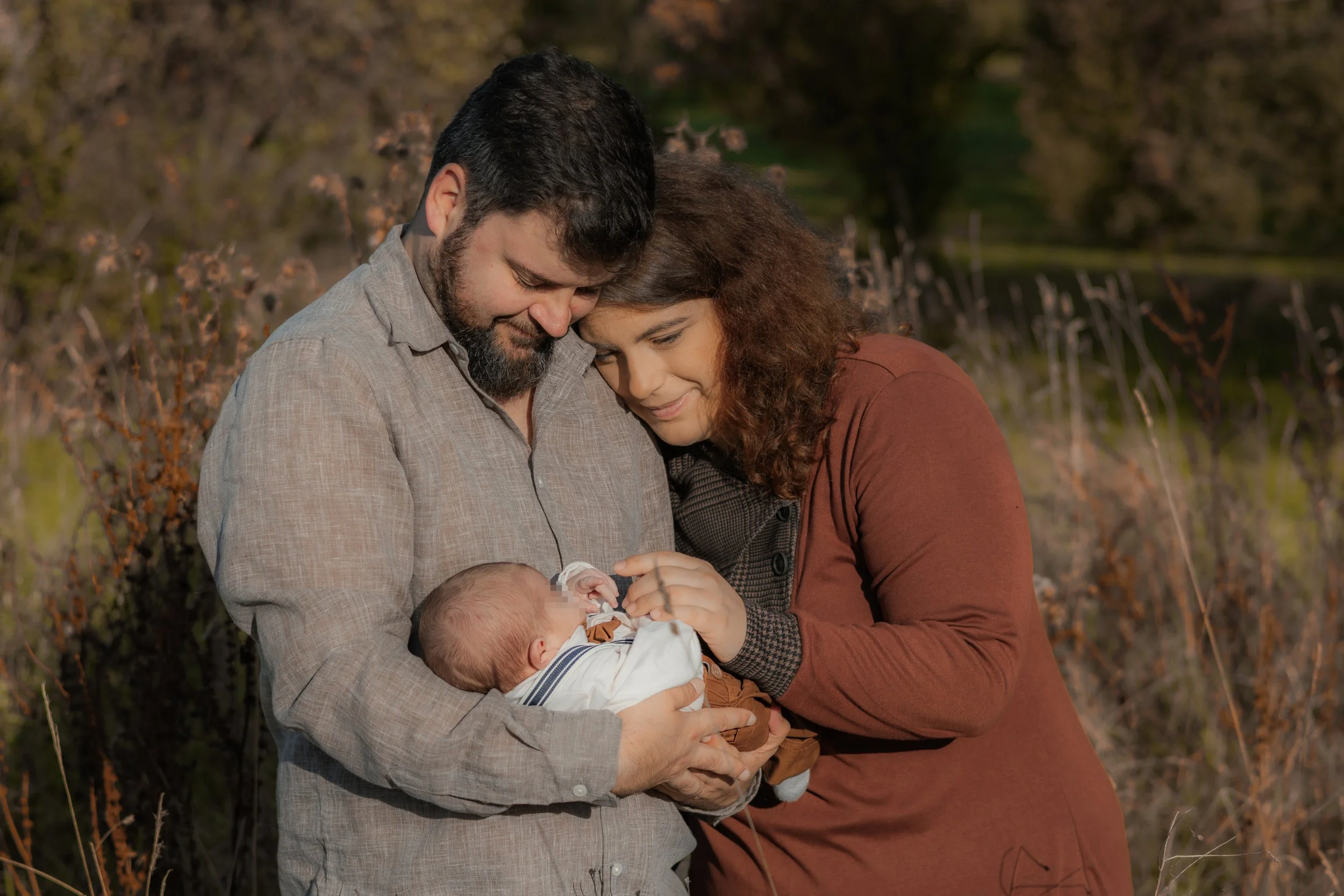 Ein Paar hält ein neugeborenes Baby und blickt liebevoll auf das Kind, im Freien bei Sonnenuntergang.
