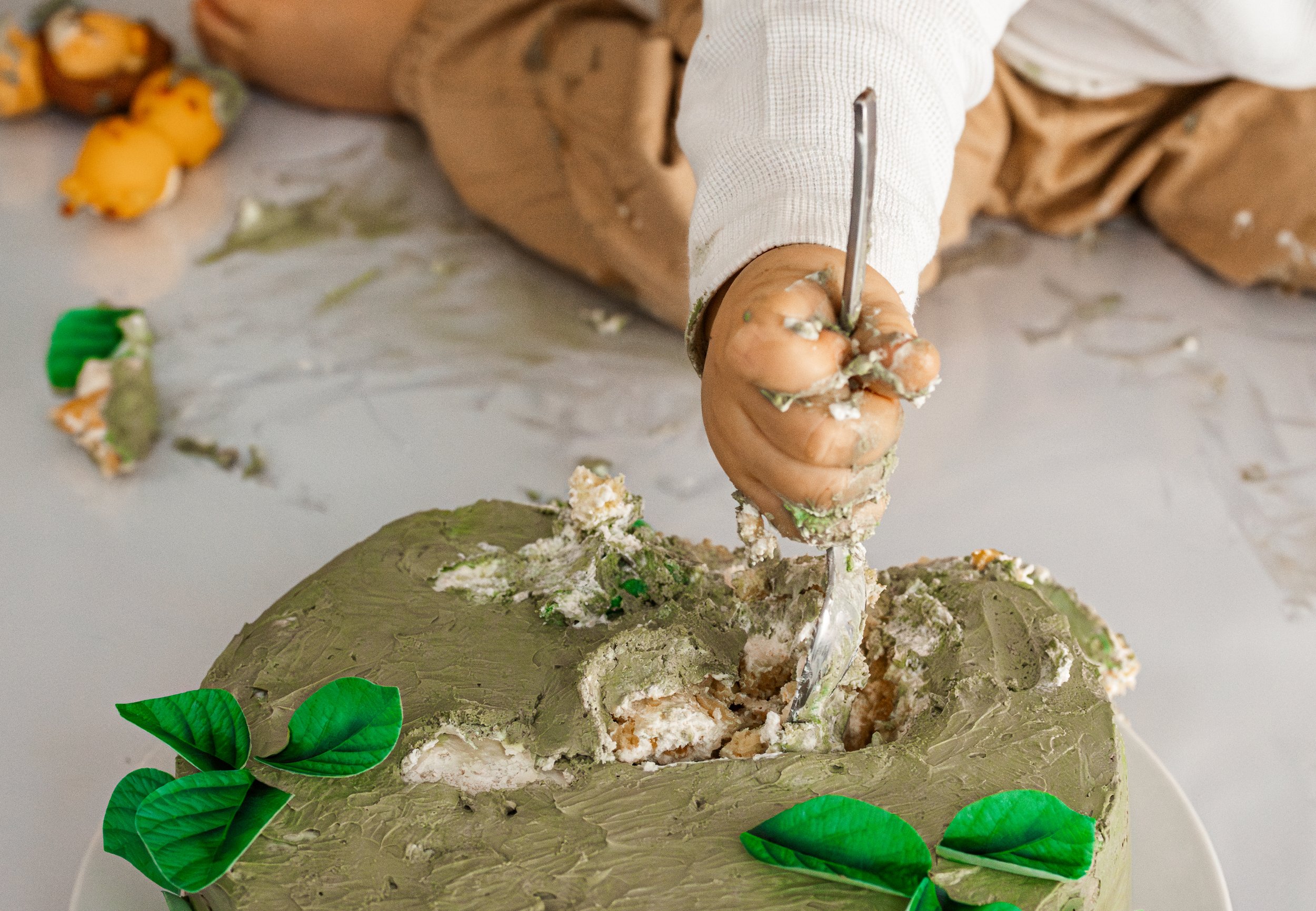 Eine Person schneidet eine grüne, pflanzenartige Torte mit einem Messer. Die Torte ist mit grüner Glasur bedeckt und mit grünen Blättern dekoriert.