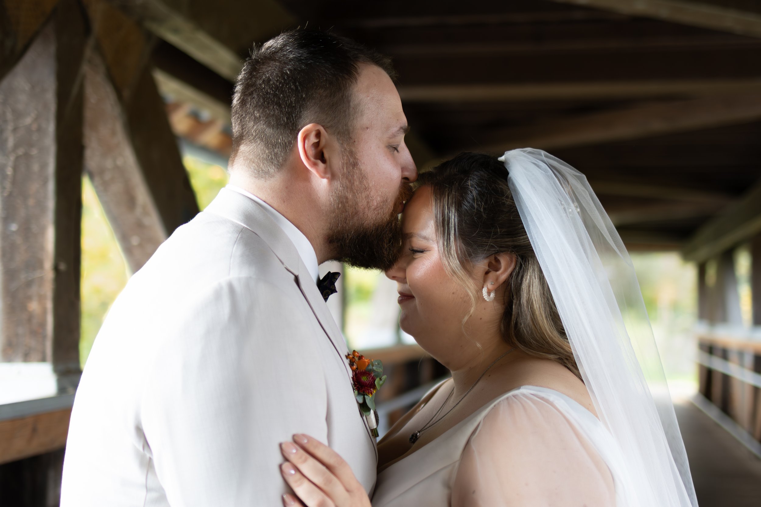 Ein Brautpaar im Hochzeitskleid und Anzug küsst sich auf einer Holzbrücke.