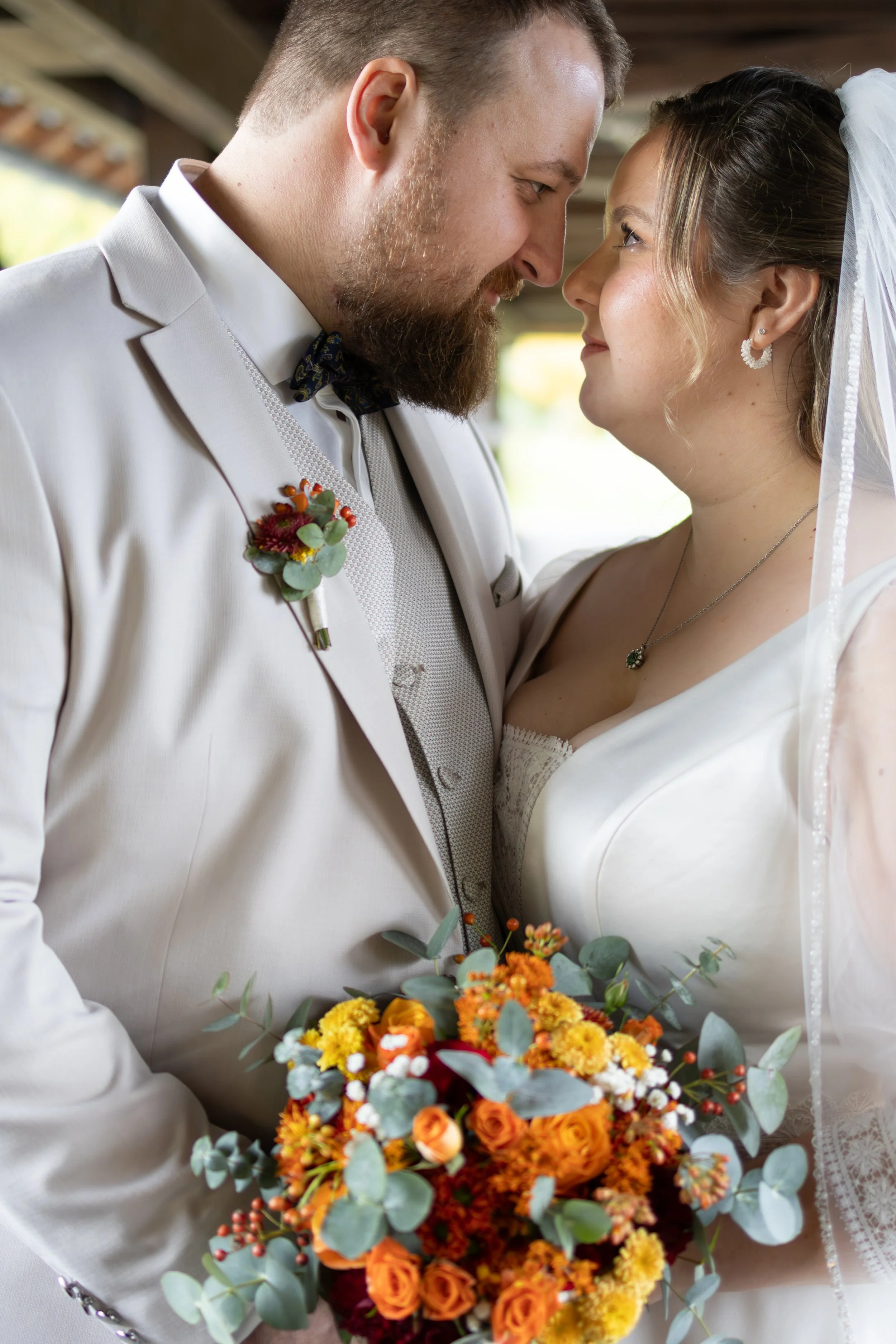 Ein Brautpaar bei einer Hochzeit, sie stehen sich gegenüber, lachen und halten eine Blumenstrauß mit orange und gelben Blumen.