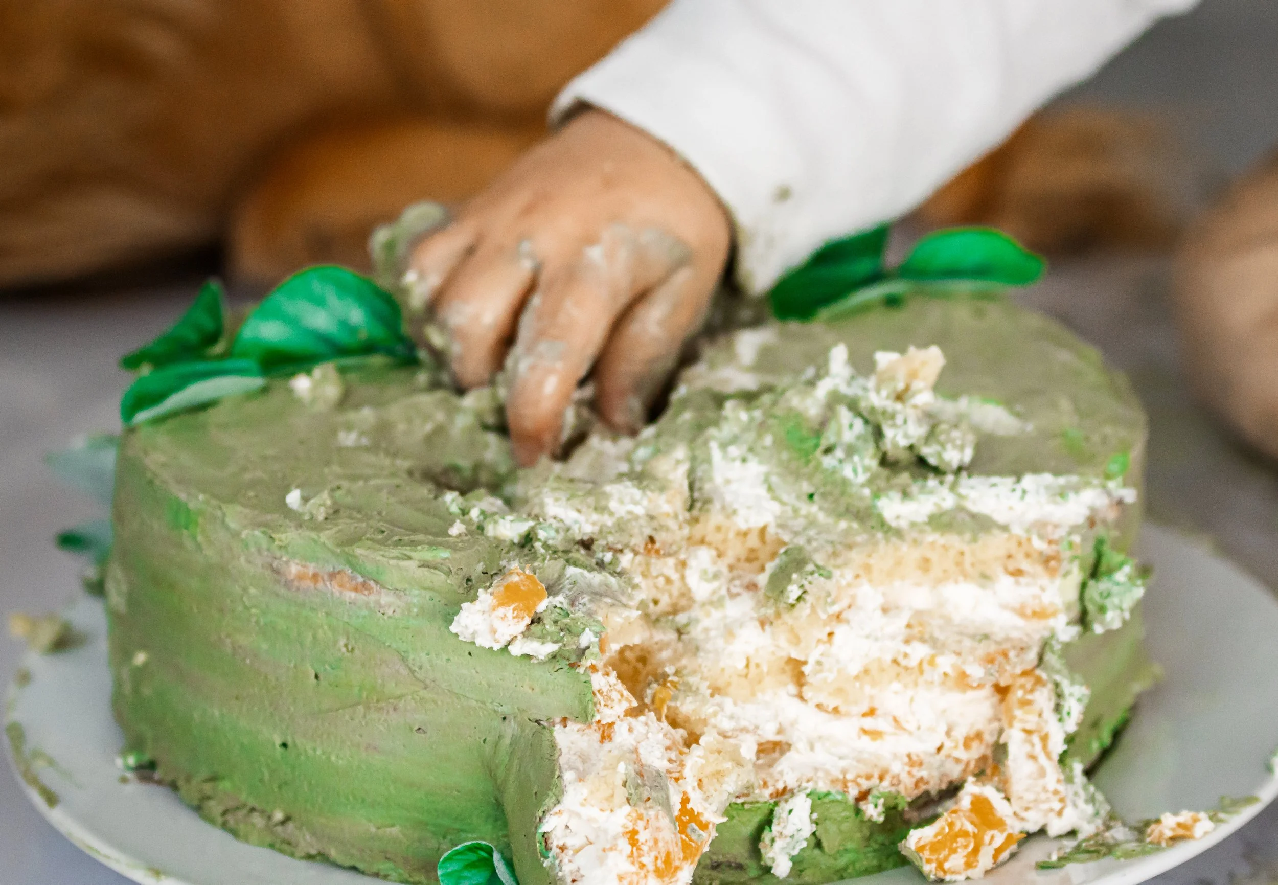 Hand, die grüne und weiße Creme auf einem großen, halbfertigen Kuchen verteilt, während die Person den Kuchen beim Dekorieren mit grünen Dekorationen abschließt.