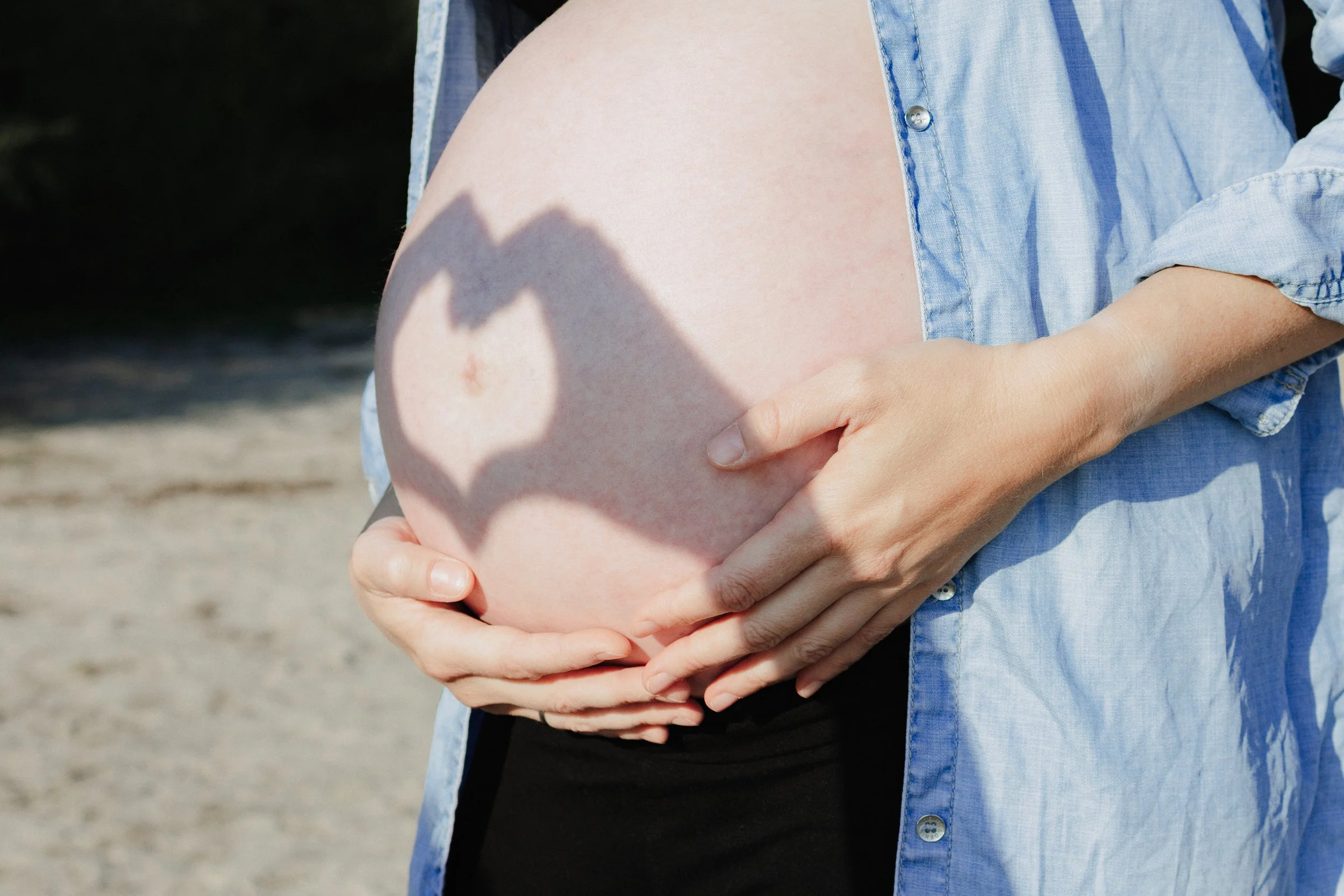 Schwangere Frau, die ihren Babybauch im Freien hält, mit Schatten von Herz auf Bauch.