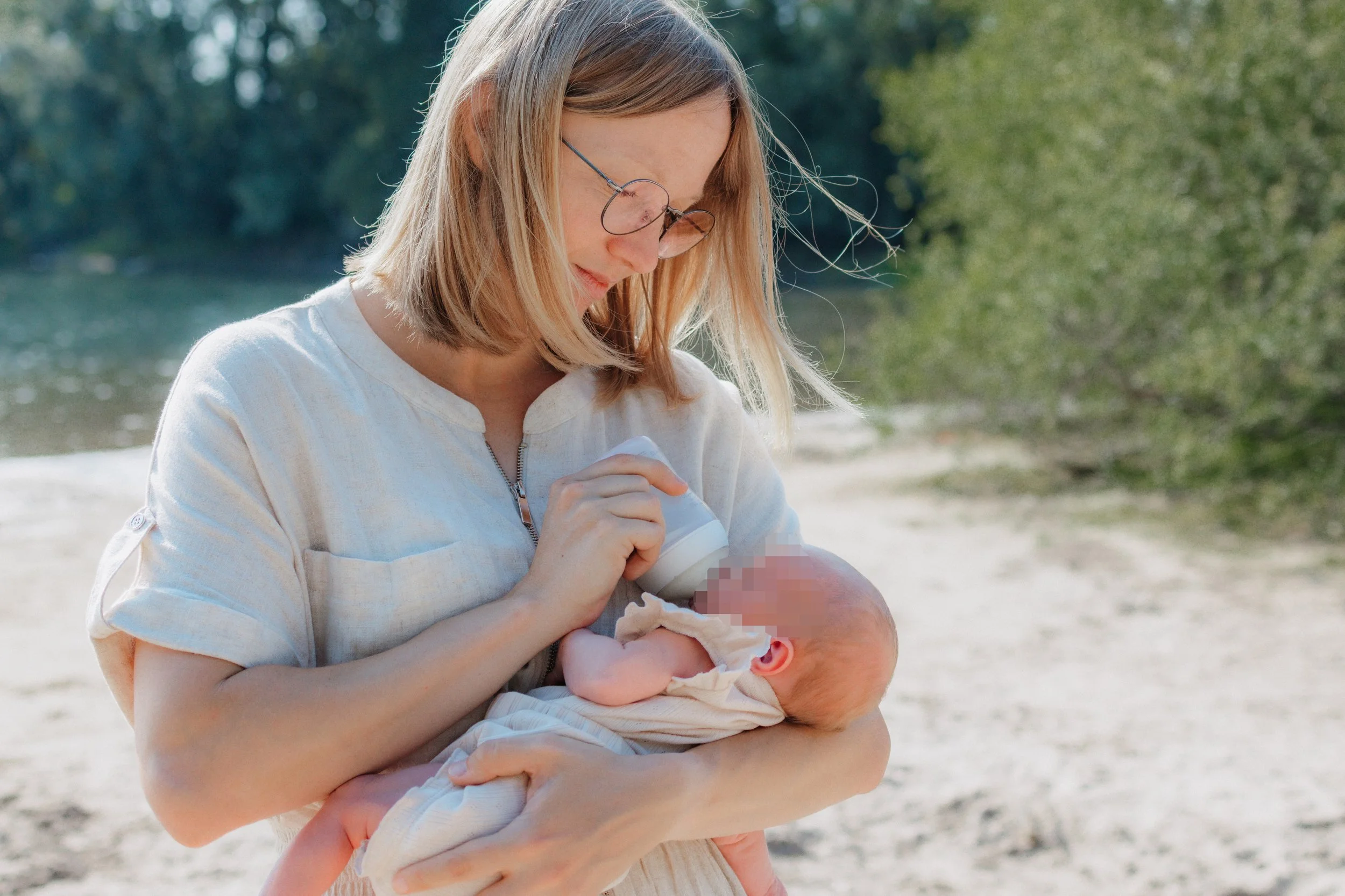 Frau füttert ein neugeborenes Baby mit einer Flasche am Flussufer im Freien.