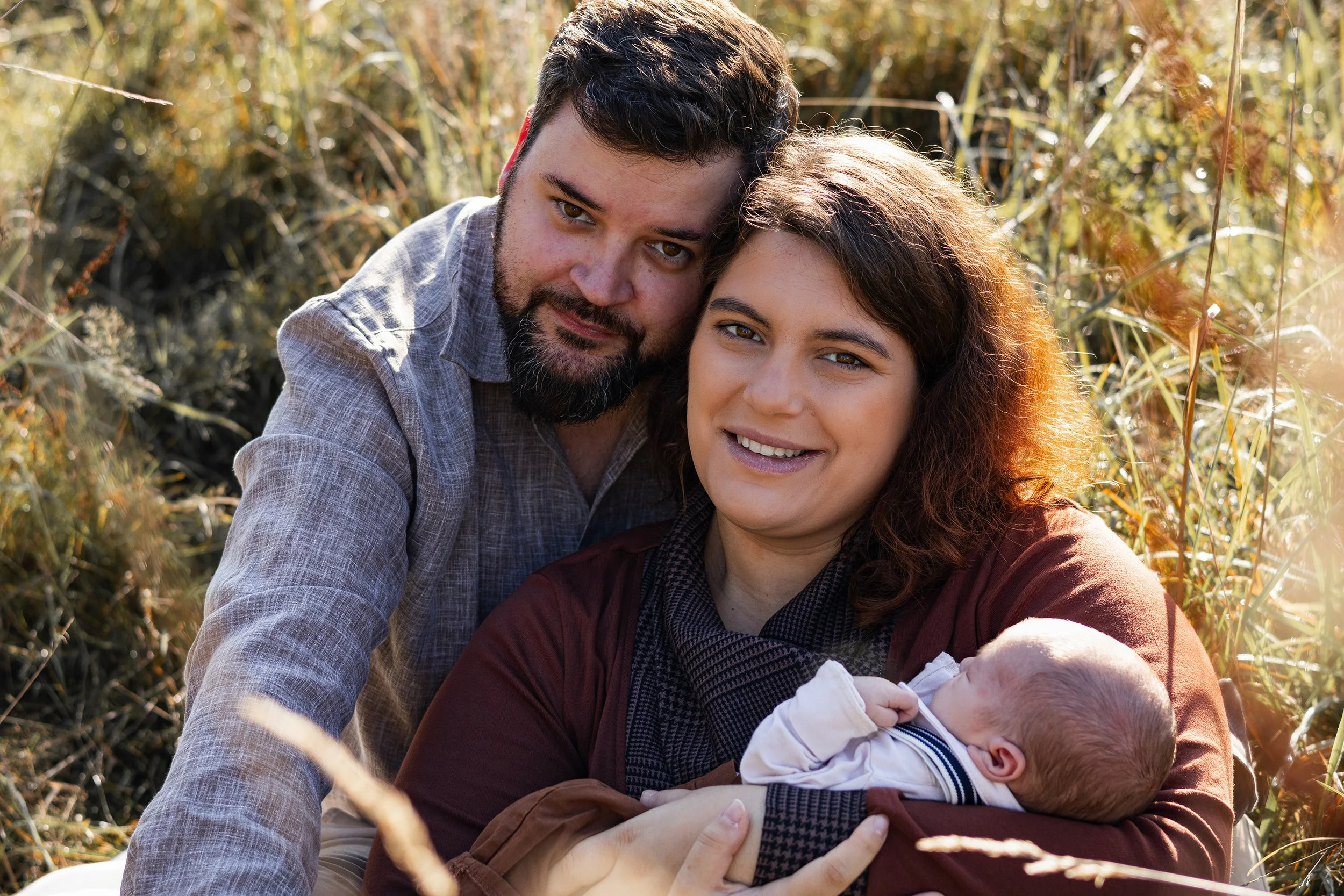 Eine glückliche Familie mit einem Mann, einer Frau und einem Baby, die im Freien in einem Feld sitzen und die Sonne genießen.