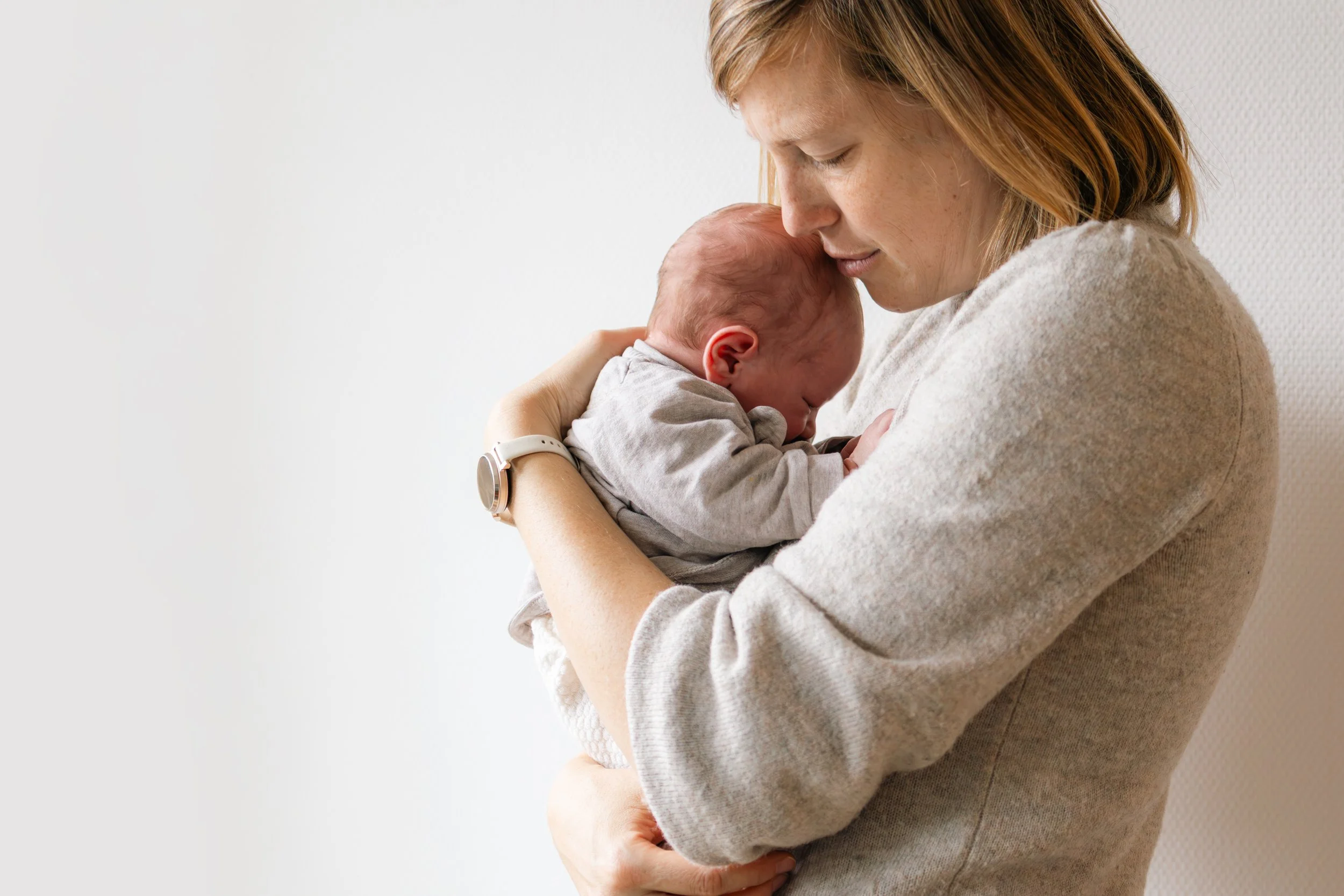 Eine Frau hält einen Neugeborenen liebevoll im Arm, die Stirn an die des Babys gelegt.