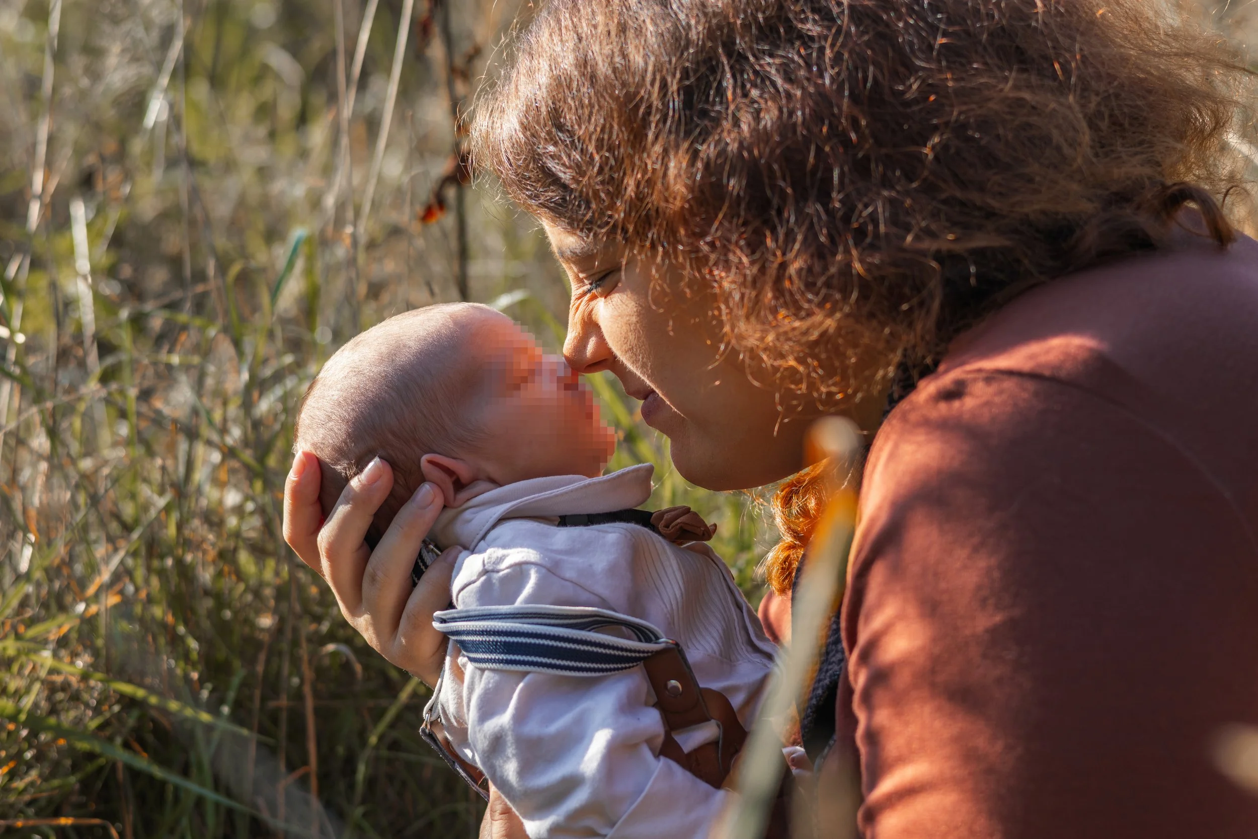 Eine Frau hält ein Baby in den Händen und zeigt ihm Liebe, während sie sich im Freien in einem Feld oder Wald befindet.