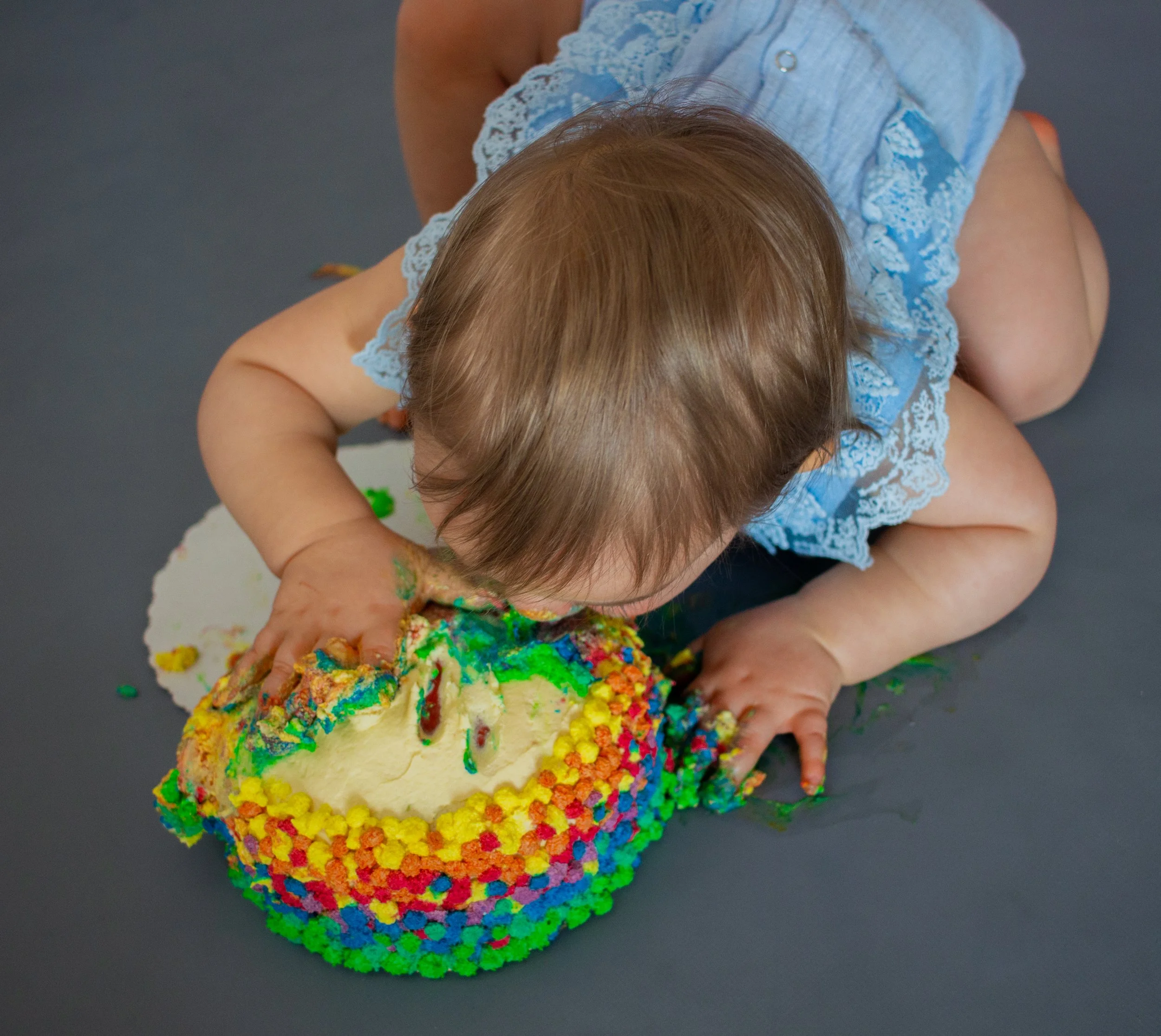 Ein Baby beim Ertasten und Spielen mit einem bunten, mit Zuckerguss und Kandistropfen verzierten Geburtstagskuchen.