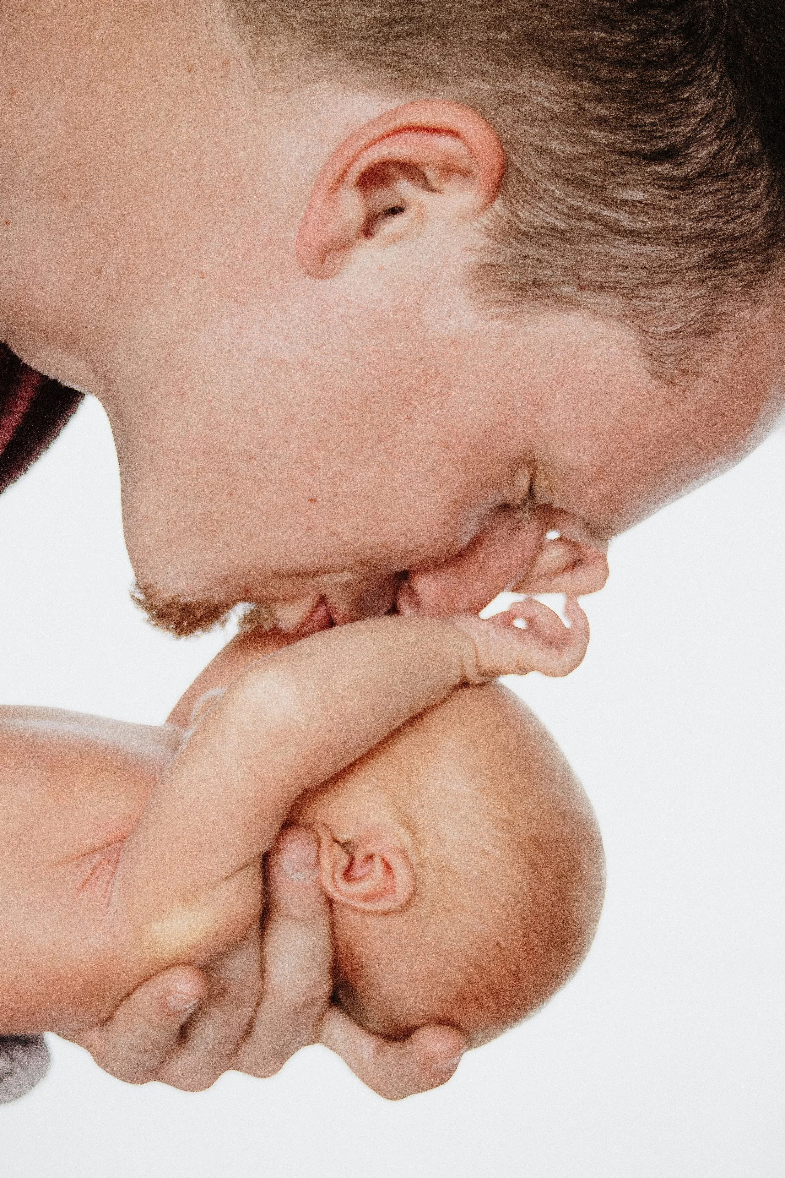 Ein Mann hält ein neugeborenes Baby in den Händen und küsst es auf die Stirn.