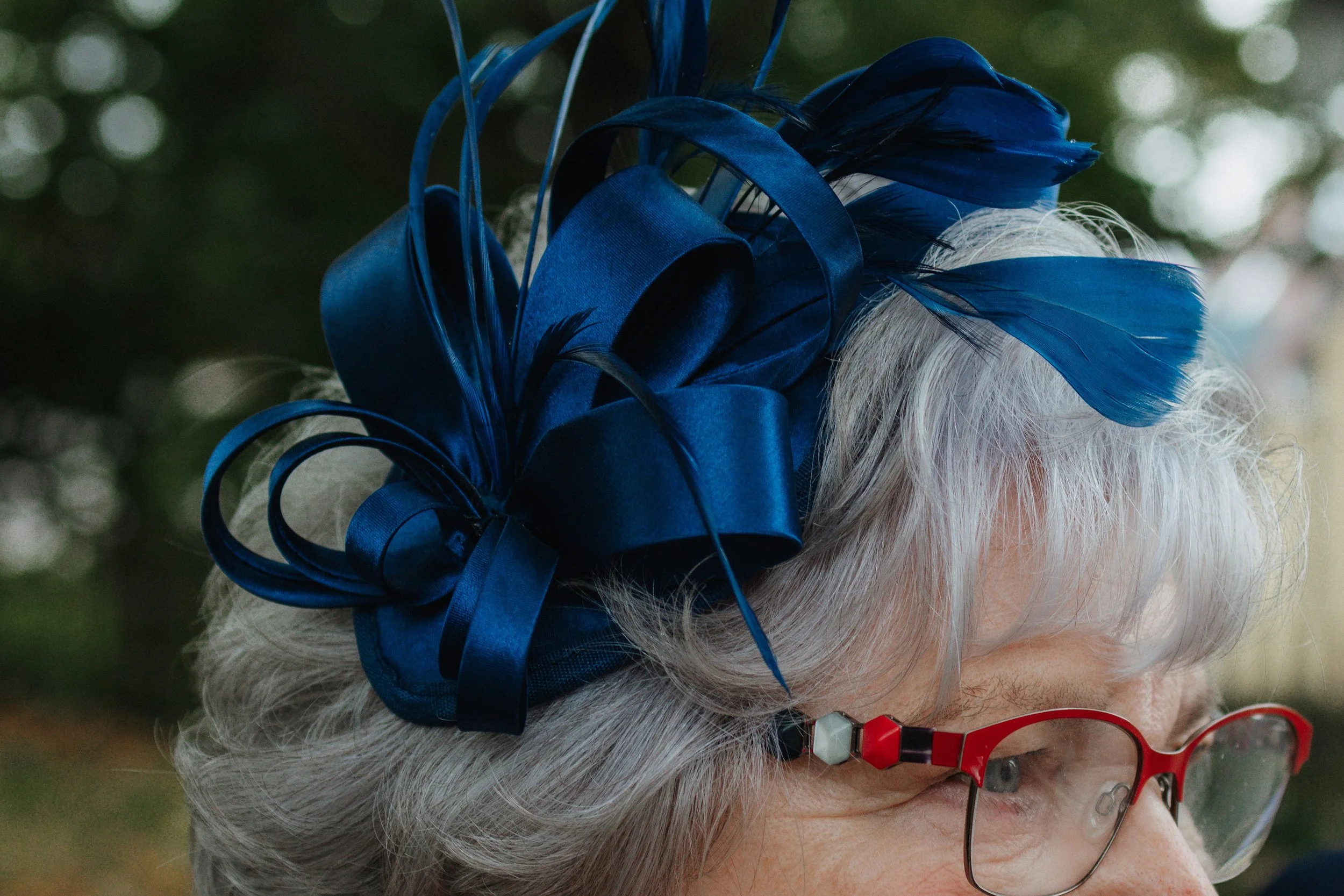Oma mit blauer Hutdekoration aus Federn und Schleifen, trägt rote Brille