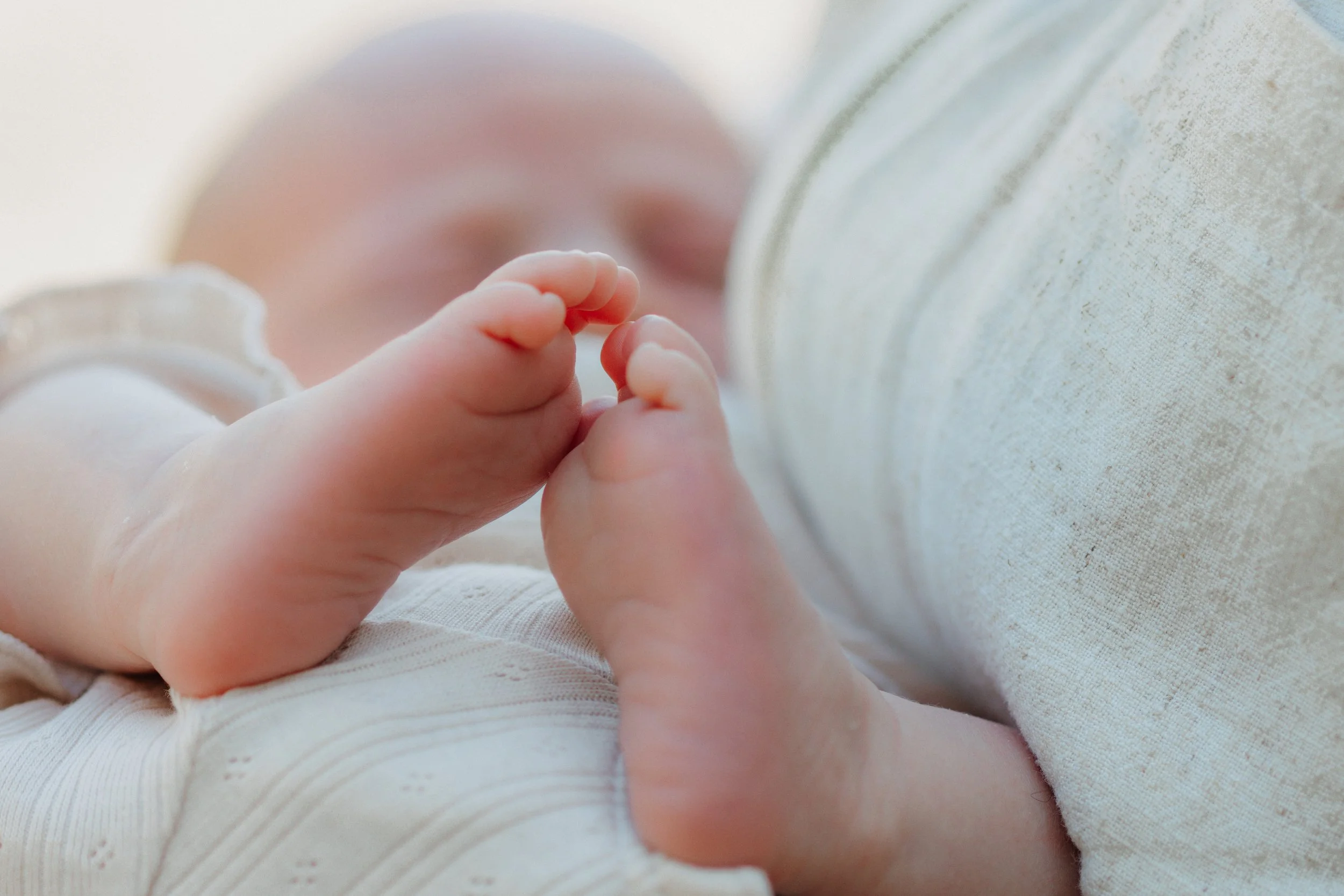 Nahaufnahme eines schlafenden Babys, das eine Hand an seinen Mund hält, auf einem Bett liegt.